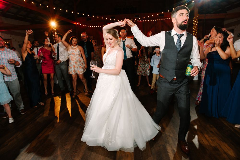 String lights illuminate an outdoor wedding reception dance floor with guests dancing and celebrating.