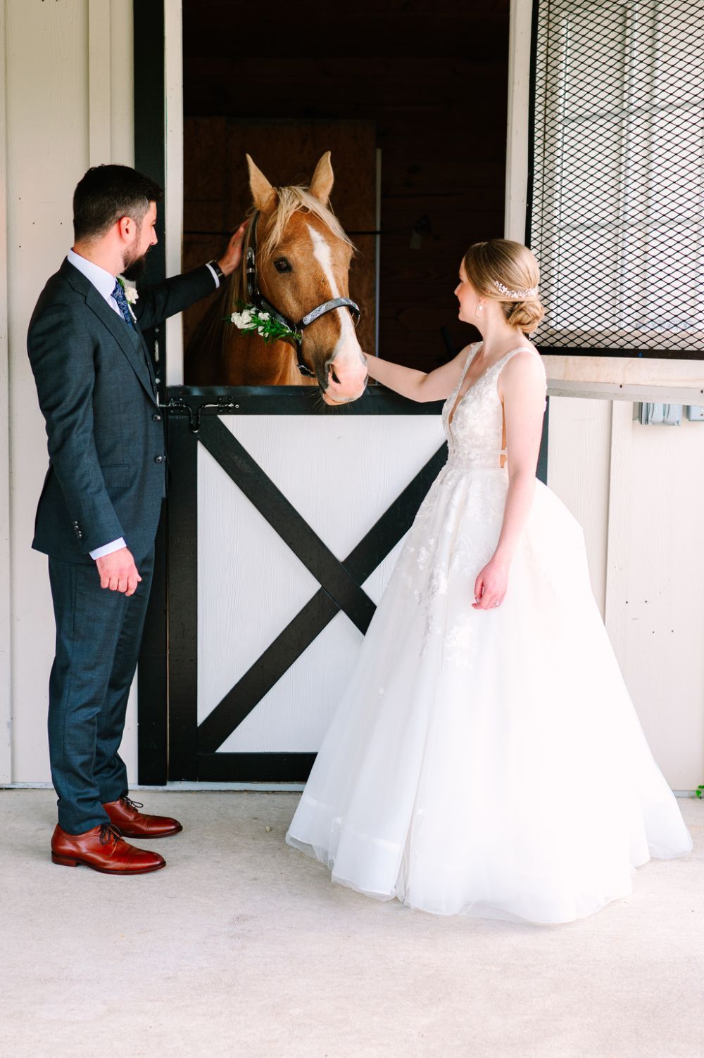 Wedding party posing by white horse stables with formal attire and black doors.