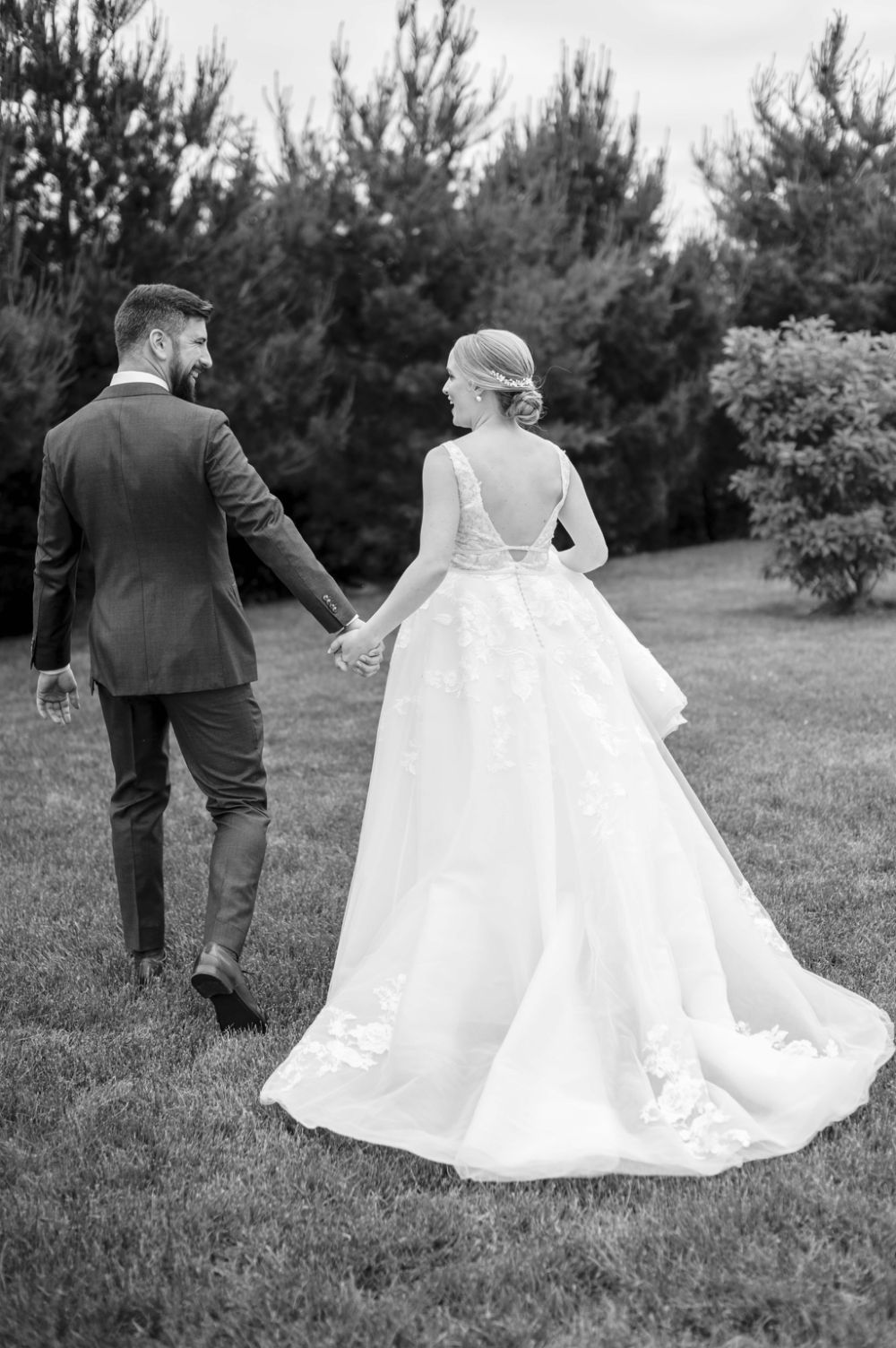 Black and white photo of newlyweds walking together through a pine tree garden.