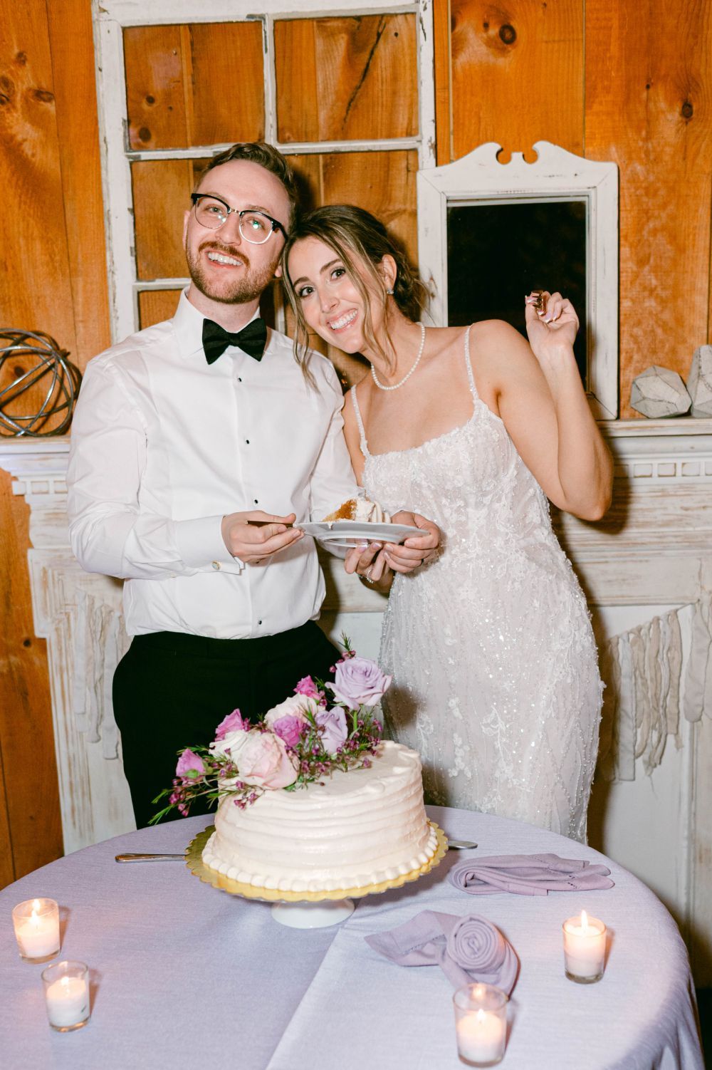 Couple cutting their wedding cake at a reception with candlelit table setting.