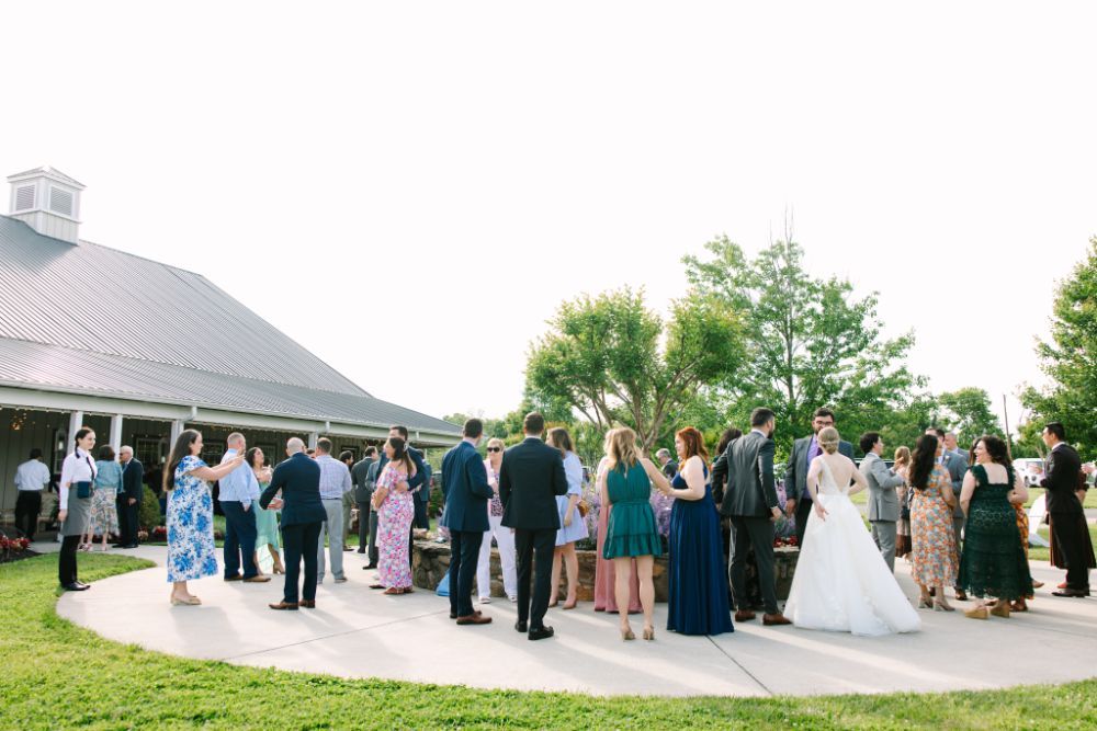 Panoramic view of wedding guests mingling on an outdoor patio at sunset against a mountain backdrop.