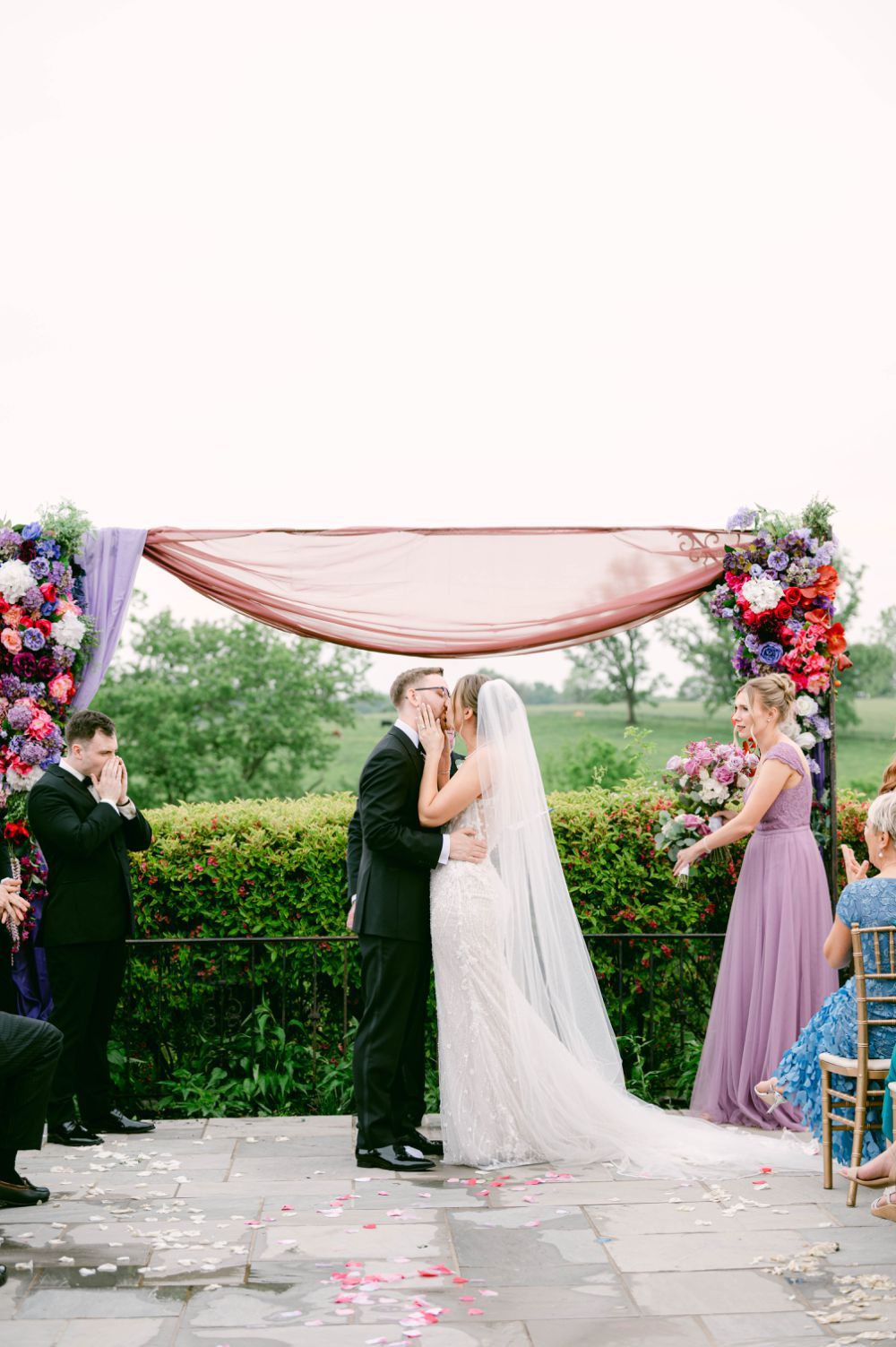 Wedding ceremony setup outdoors featuring a flowing pink canopy and rose petals scattered on the stone pathway.