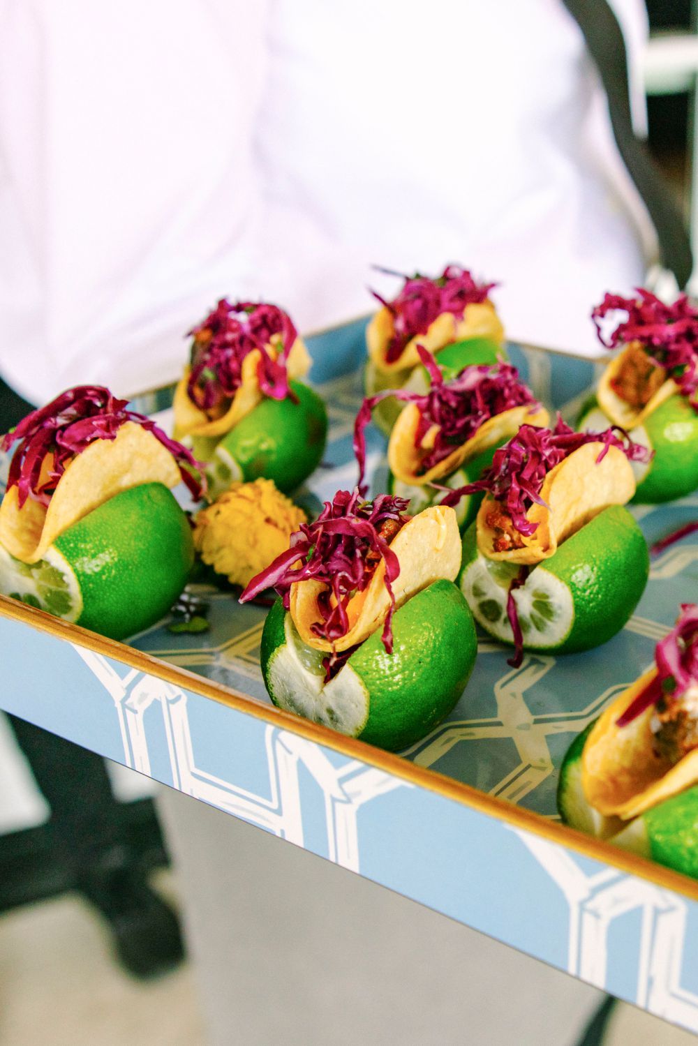 Fresh lime cups filled with appetizers and topped with purple cabbage served on a decorative tray.