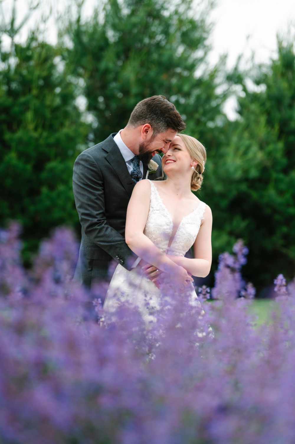 A romantic couple shares an intimate moment surrounded by blooming purple lavender flowers in a garden setting.