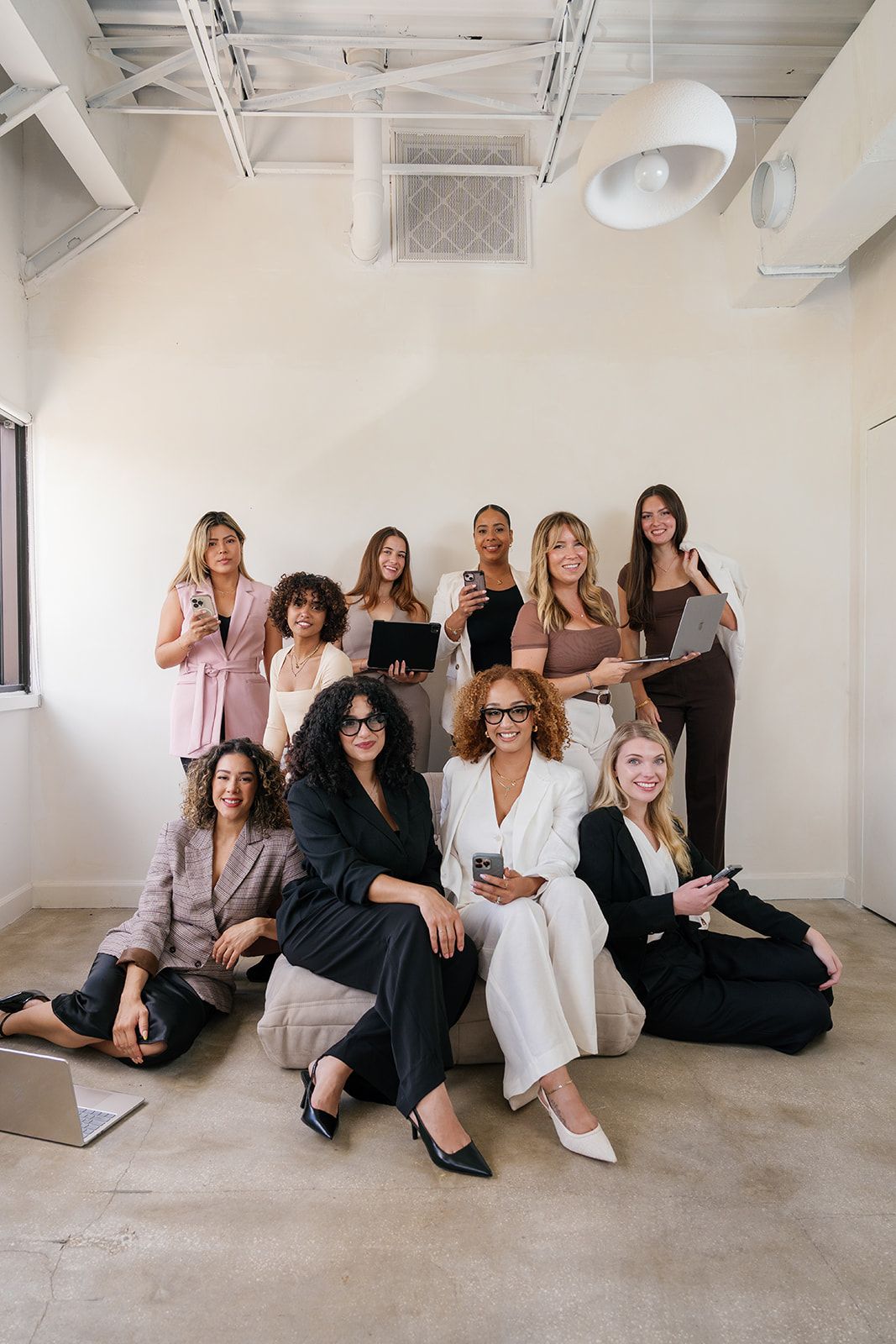 A group of professionals pose together in a minimalist white studio space with laptops and tablets.