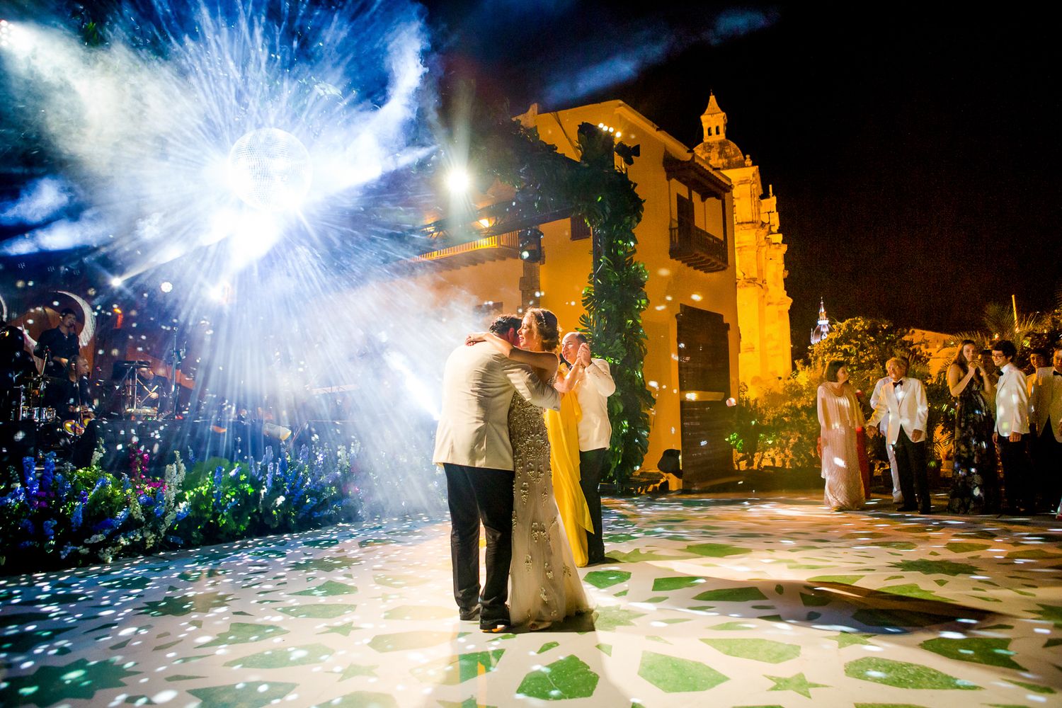 A couple dances together under bright sparklers and lights at an outdoor nighttime wedding celebration.