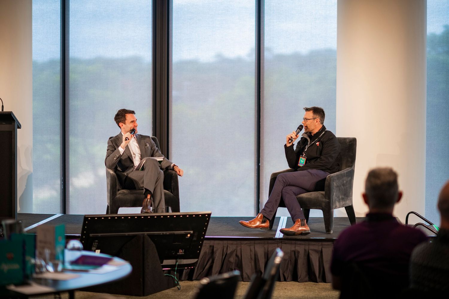 Business meeting in modern conference room with glass walls showcasing city views and multiple attendees seated at table.