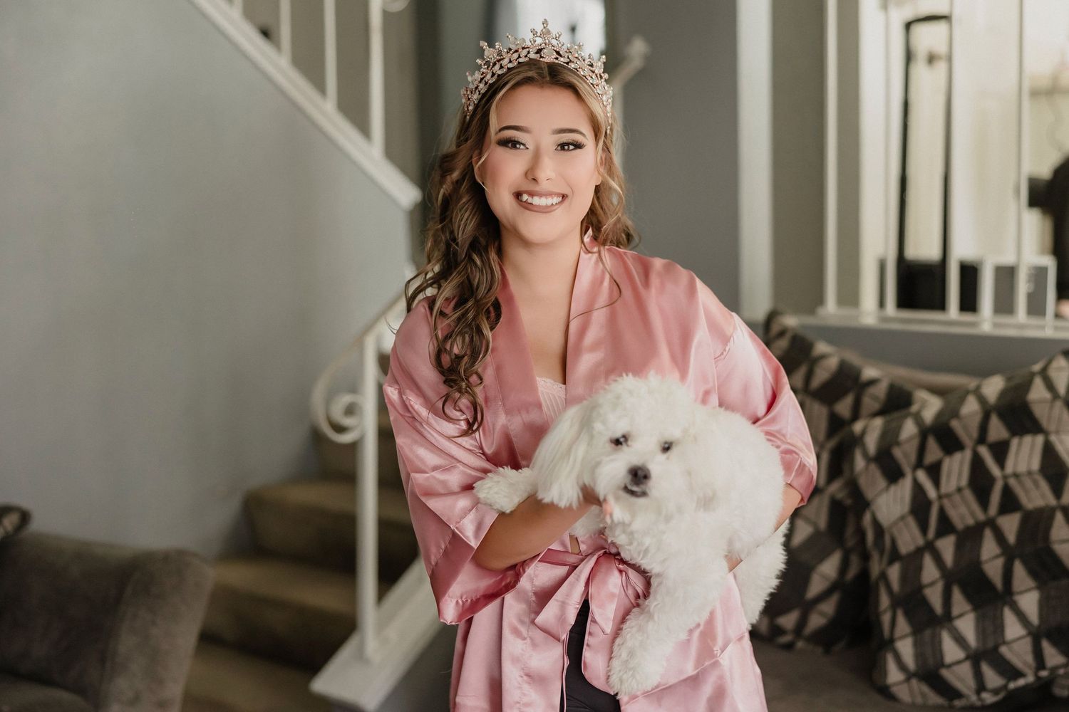 A wedding party poses with a small white fluffy dog while wearing pink and grey formal attire.