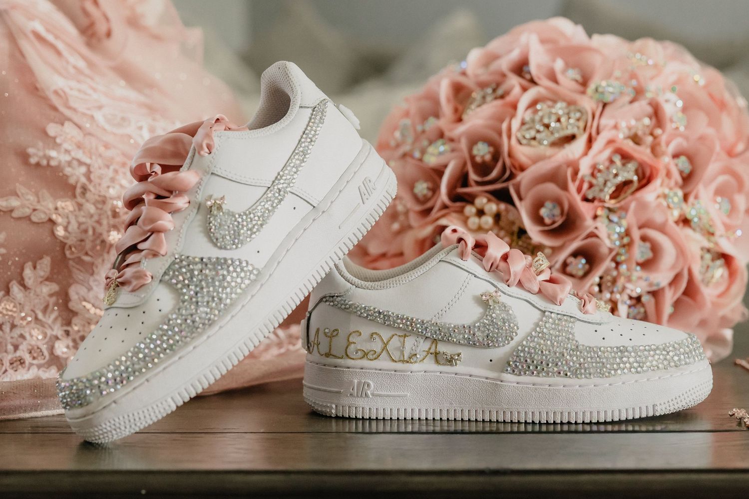 Decorative white Nike Air Force 1 sneakers with crystal embellishments next to pink roses on wooden surface.