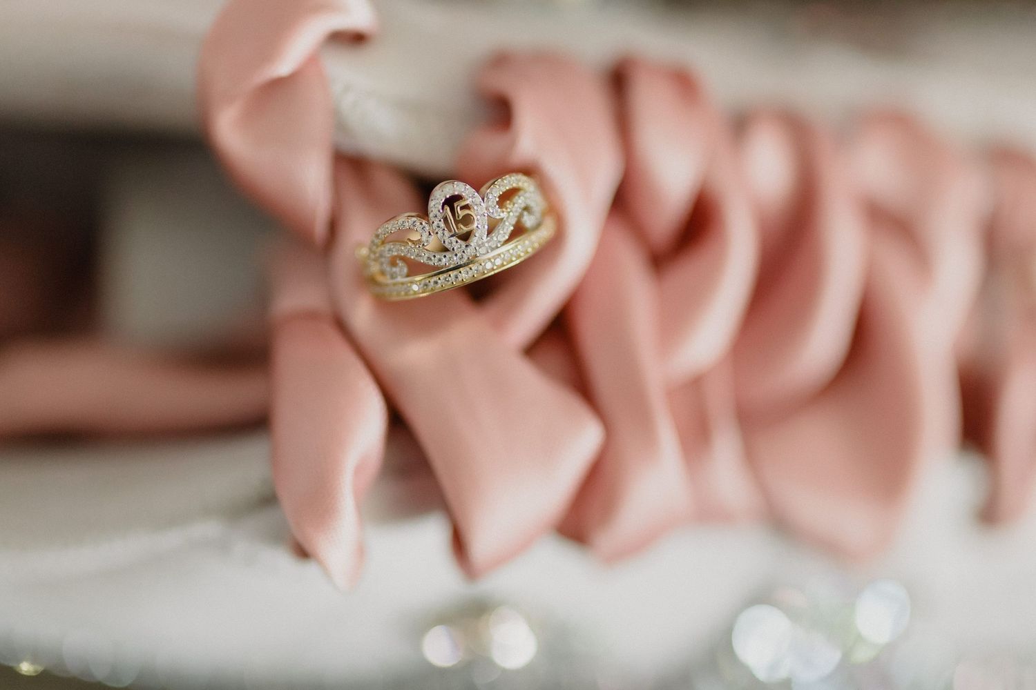 Gold wedding rings with diamonds rest against soft pink fabric in a romantic engagement setting.