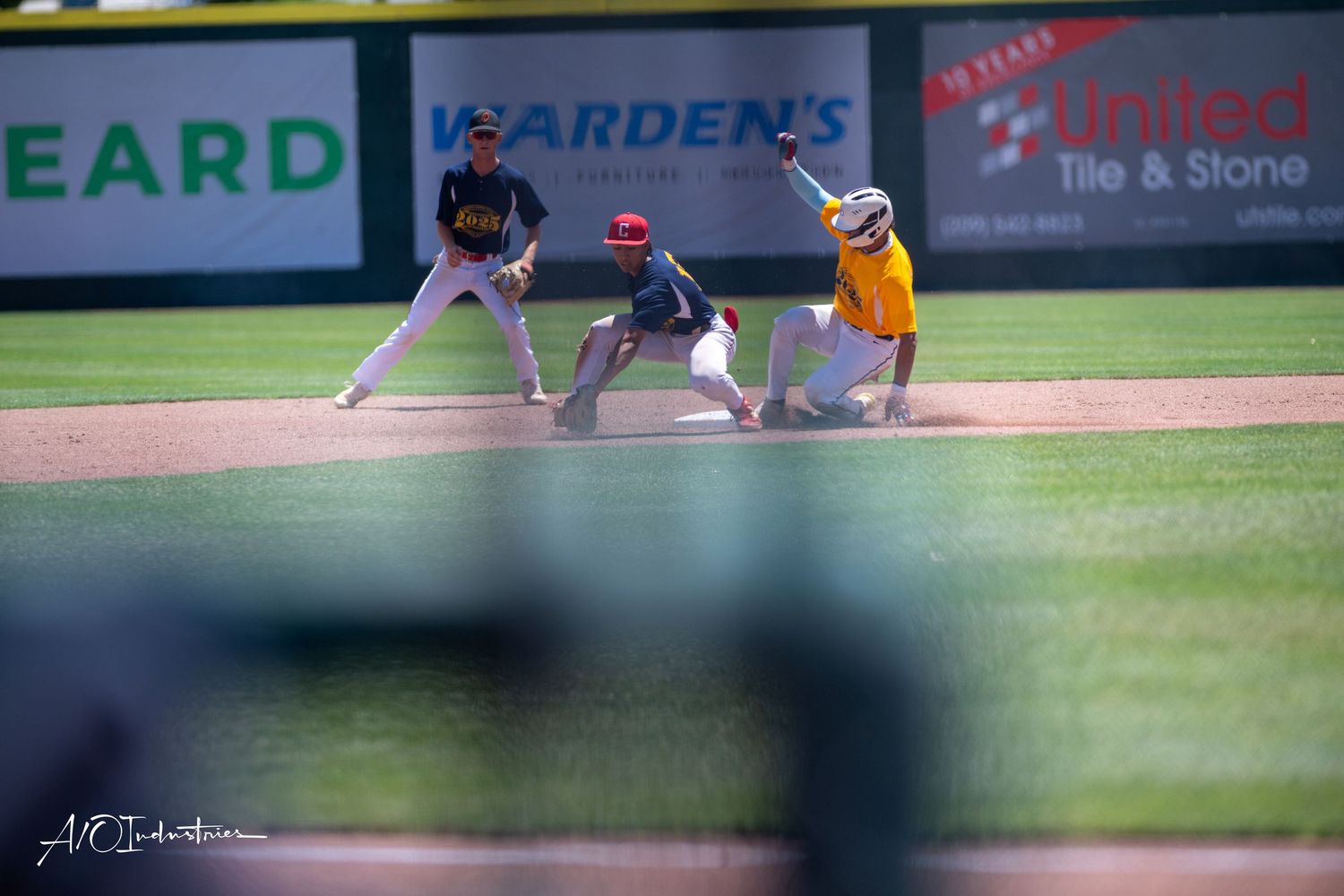 Baseball player slides into base as catcher attempts to make the tag during competitive game action.