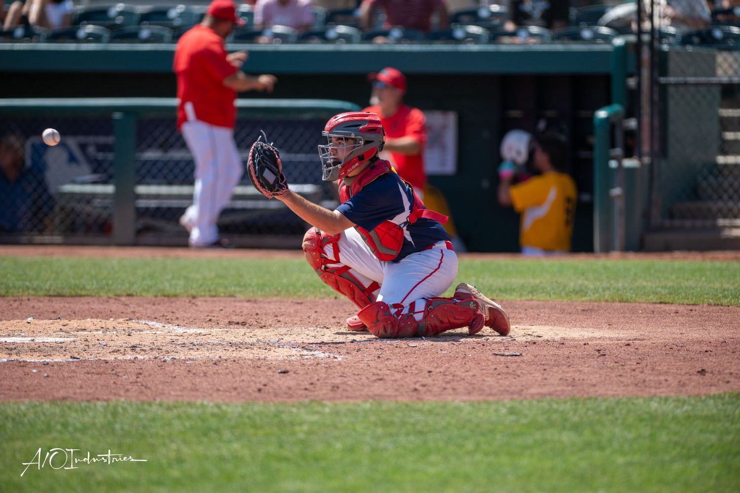 Baseball action sequence shows catcher in red uniform receiving pitch at home plate during game.