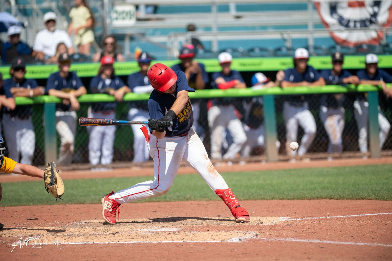 Baseball player follows through after swinging the bat at home plate during a game on a sunny day.