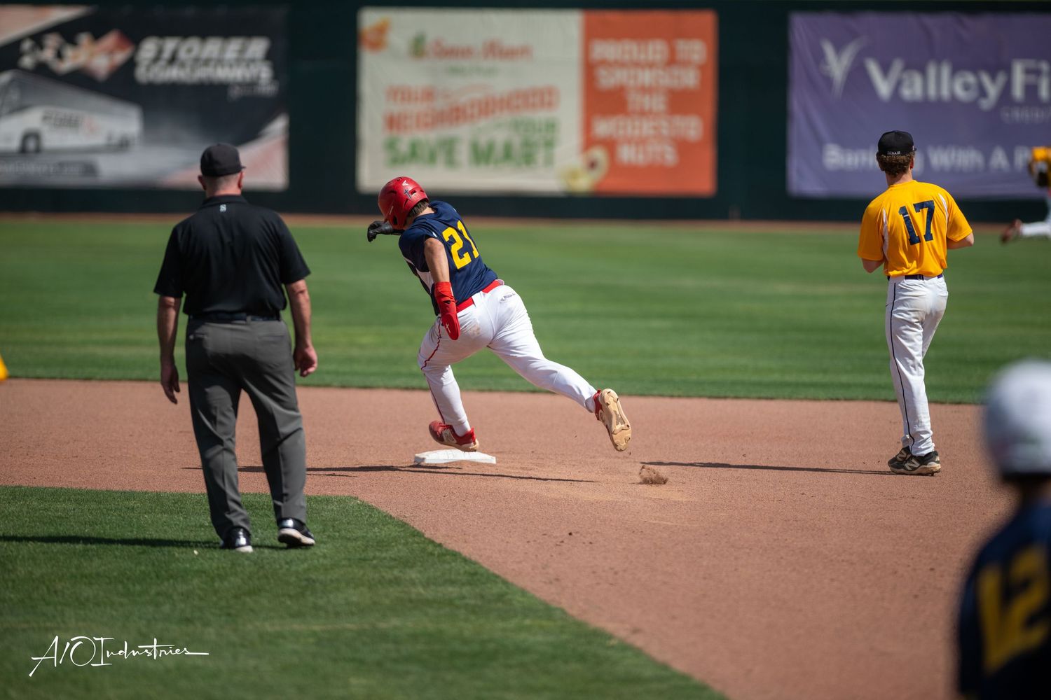 Baseball player extends to catch a ground ball during a game while umpire and opponent watch at the field.
