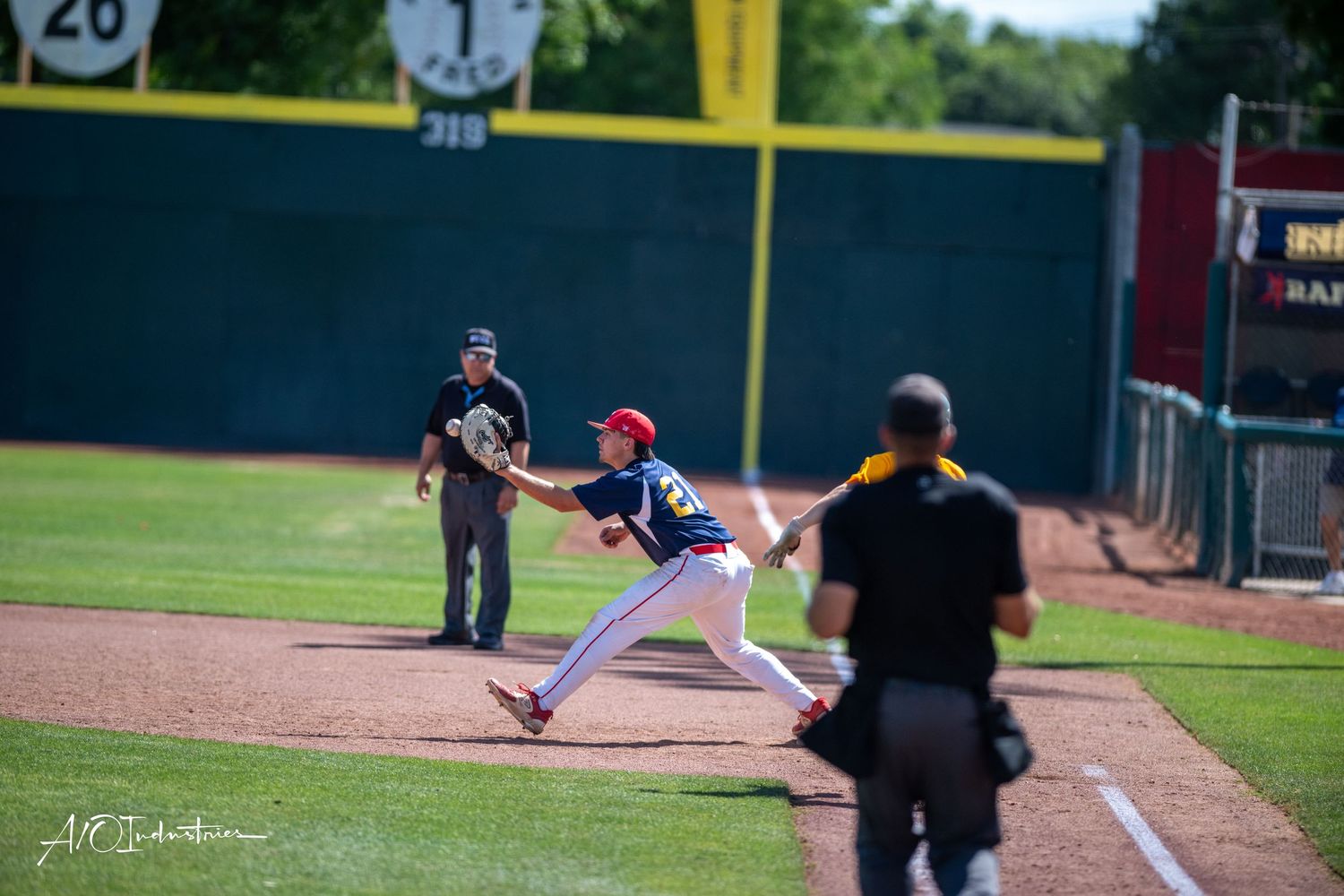 Baseball player stands at bat preparing to swing while umpire watches during game on sunny day at baseball field.