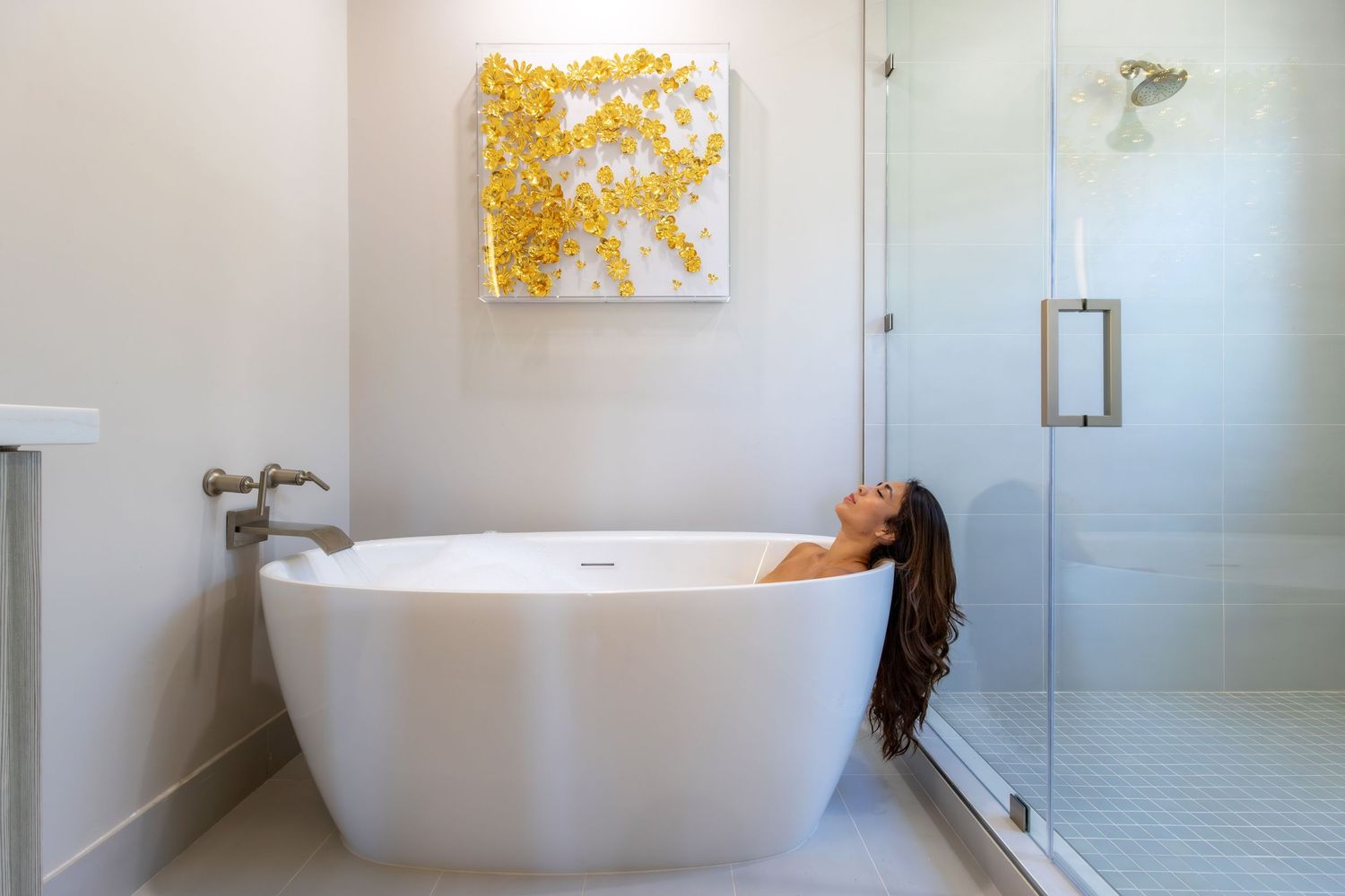 Modern white bathroom interior with freestanding tub and yellow art on wall.