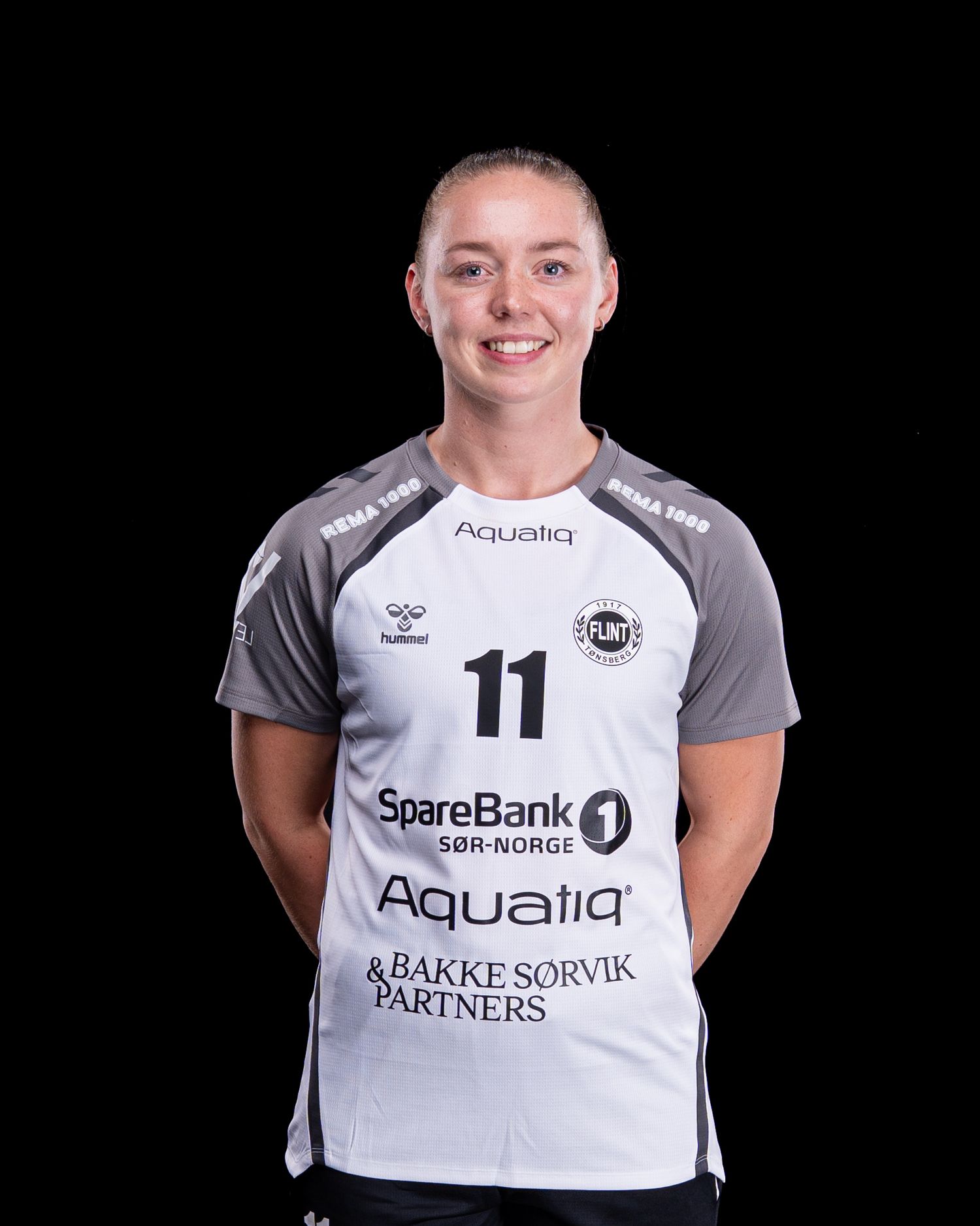 Sports player in white uniform with number 11 and sponsor logos poses for team photo against black backdrop.