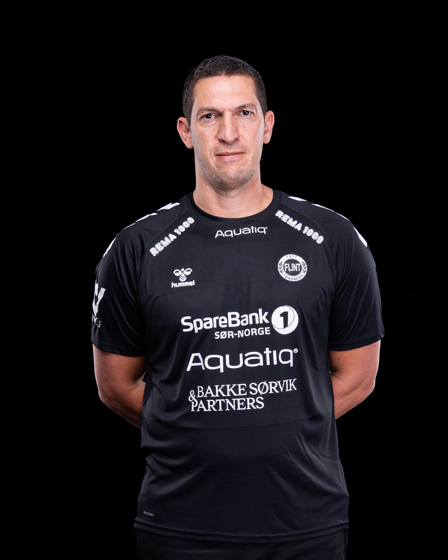 Professional athlete wearing black sports t-shirt with SpareBank and Aqualia sponsor logos against dark backdrop.