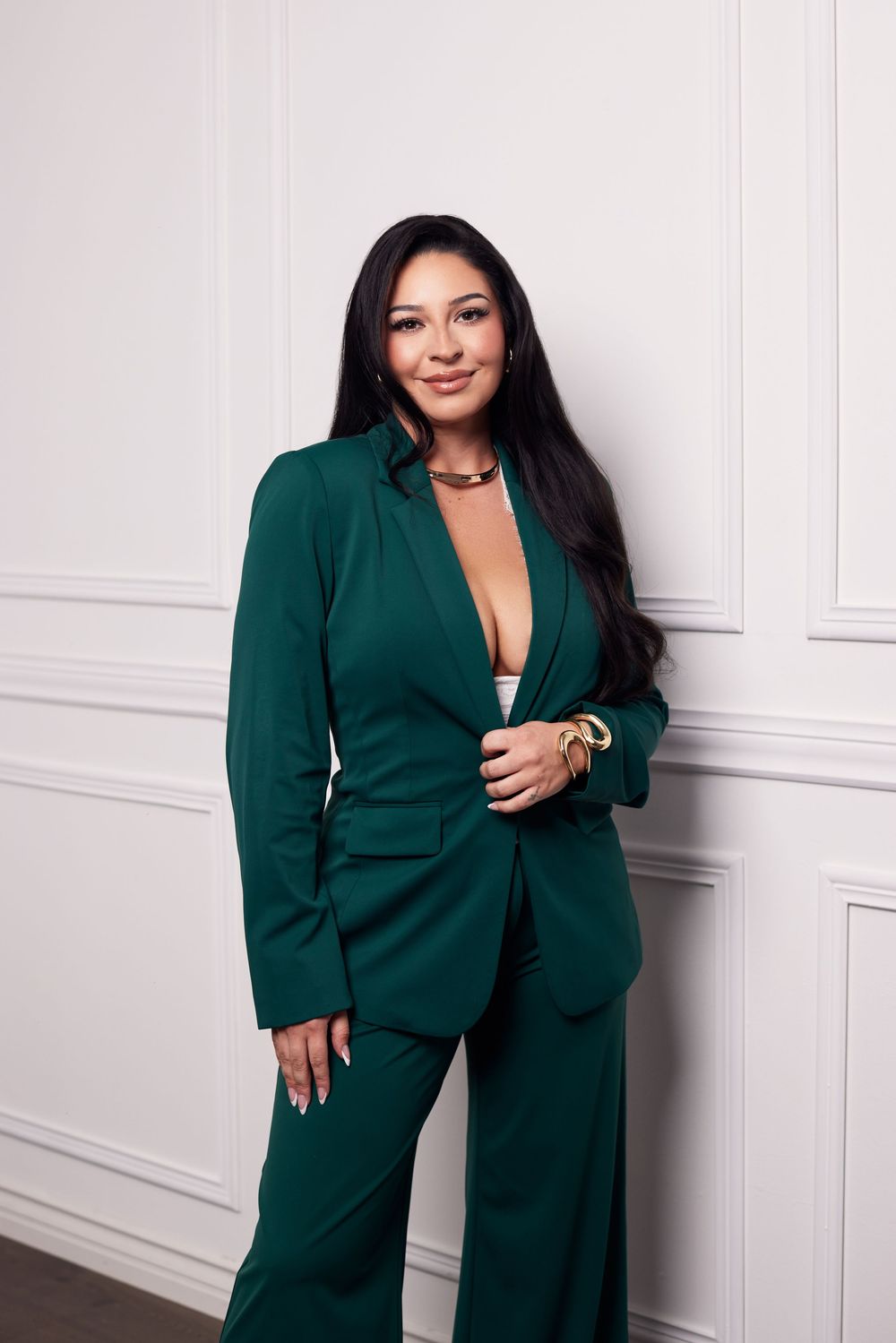 Model wearing emerald green power suit poses confidently against white paneled wall.