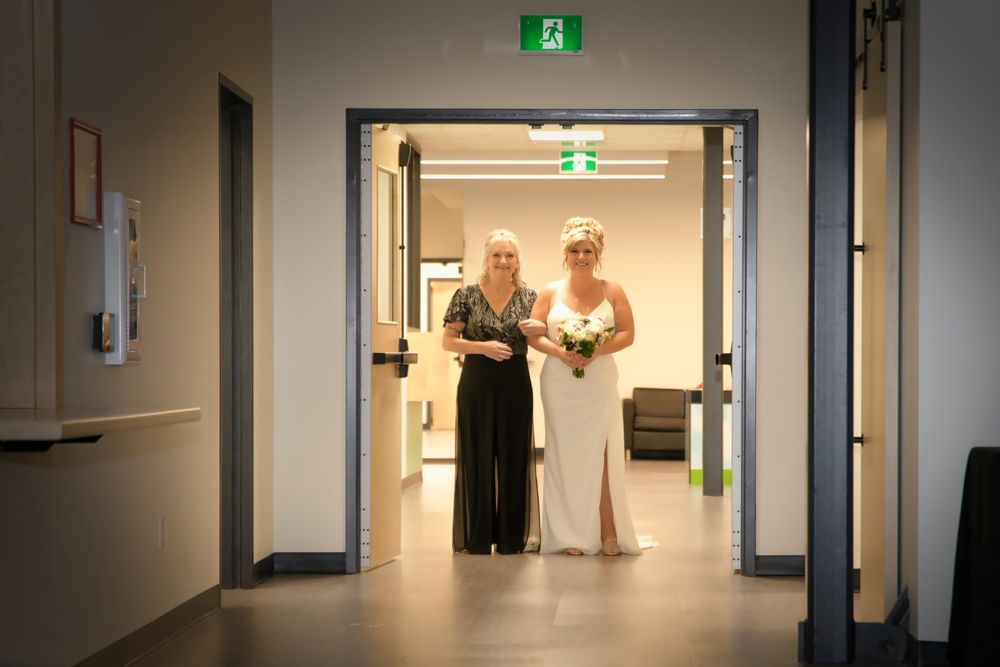 Long institutional hallway with fluorescent lighting features exit signs and safety lighting mounted along white walls.