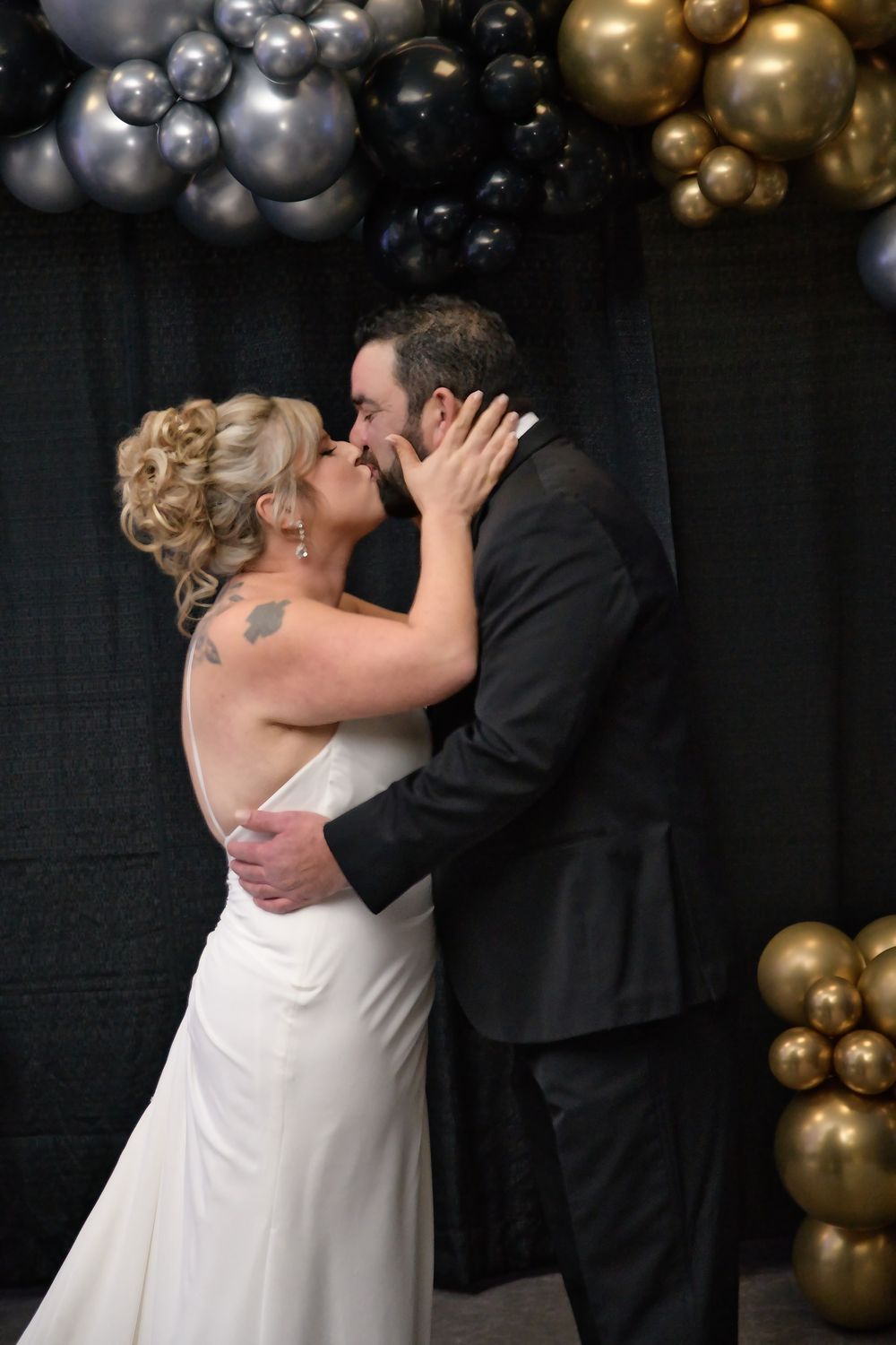 A couple shares a romantic moment surrounded by gold and silver balloon decorations.