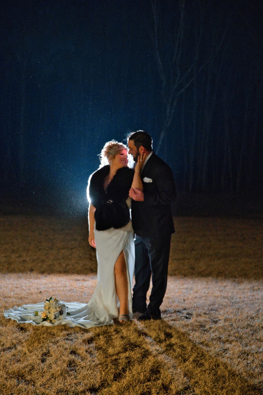 Couple shares romantic nighttime moment outdoors with dramatic backlit silhouette against dark blue sky.