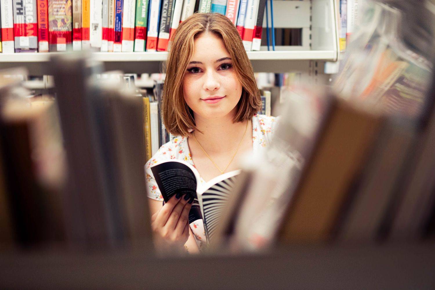 Artistic portrait taken between rows of library bookshelves with soft focus.