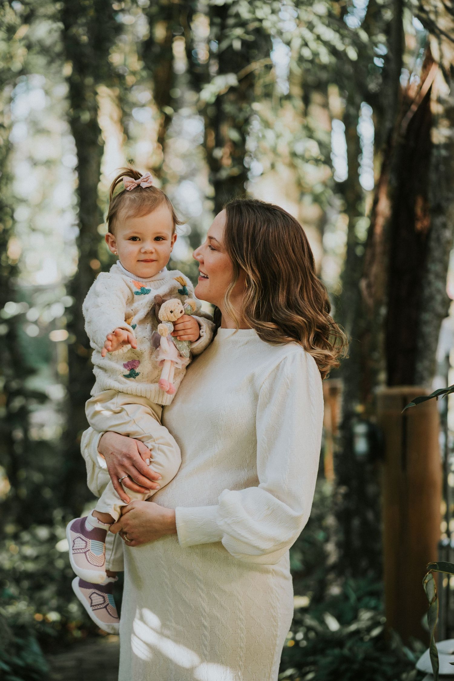 Outdoor family portrait in sunlit forest setting with soft natural lighting.