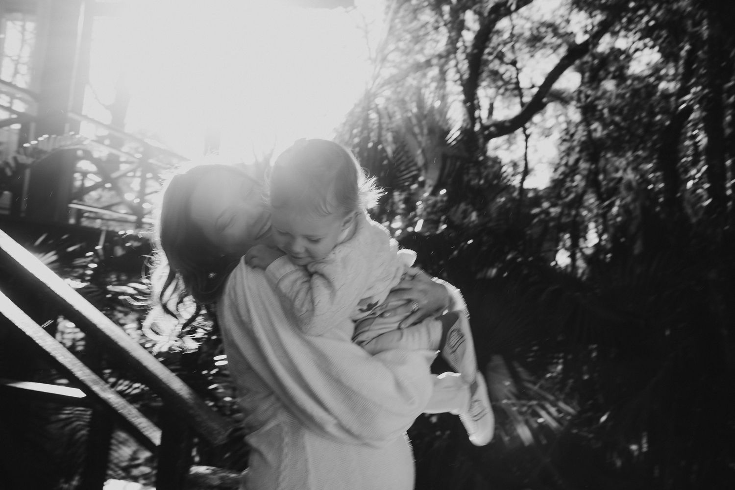 Black and white intimate moment captured in outdoor garden setting with sunlight streaming through.