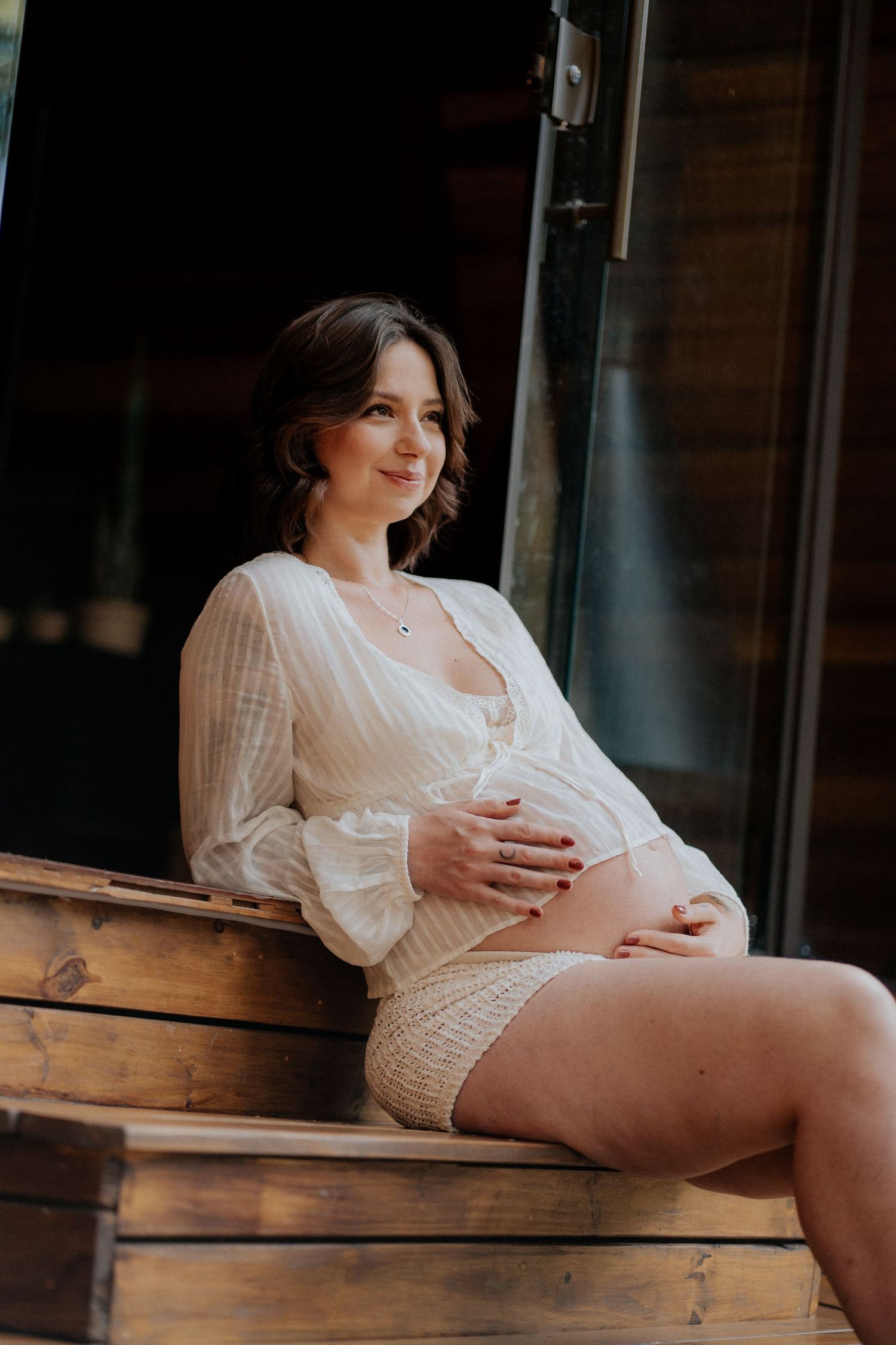 Intimate maternity portraits in white dress on rustic wooden porch.