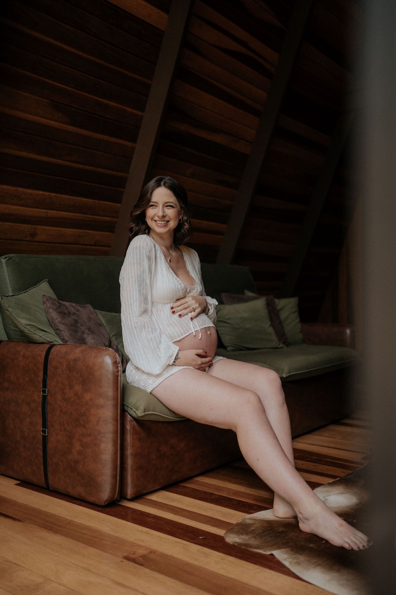 Intimate maternity portrait session on a brown leather couch in natural lighting.