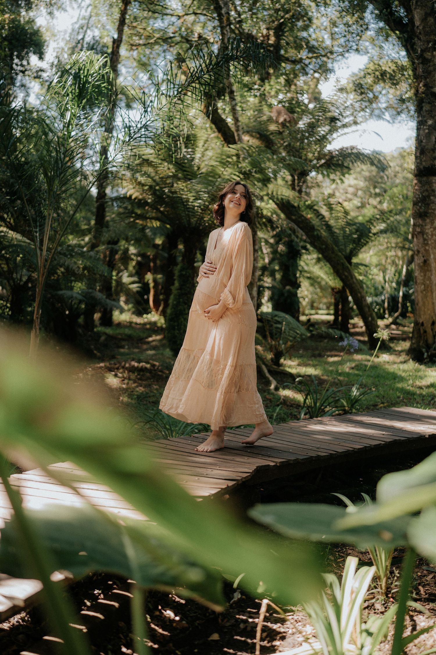 Outdoor maternity photography session on wooden walkway surrounded by lush greenery.