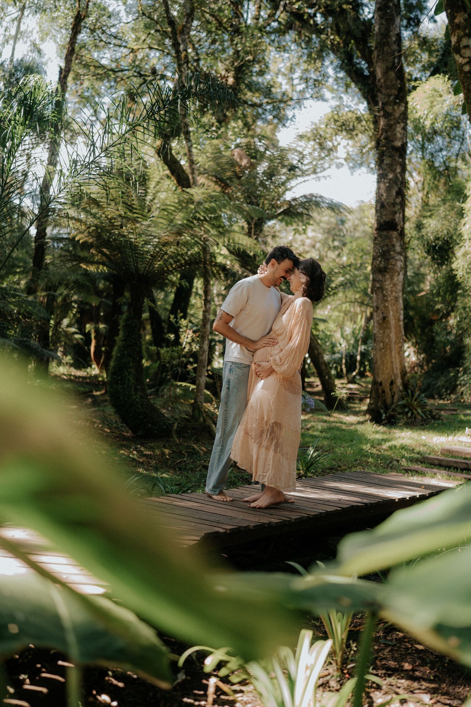Couple embraces on wooden deck surrounded by lush tropical forest in romantic outdoor photoshoot.