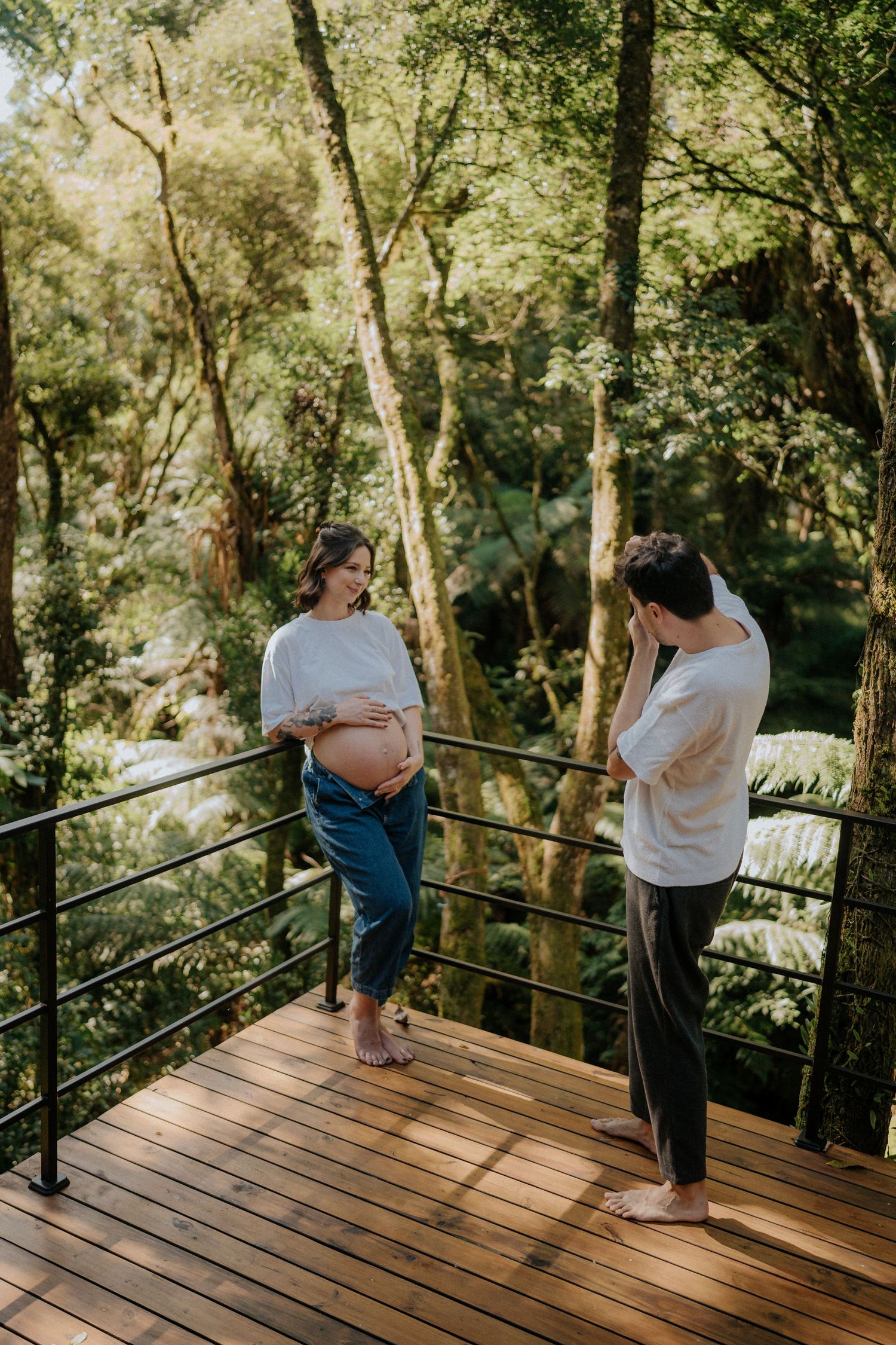 Maternity photoshoot on wooden deck surrounded by forest greenery.