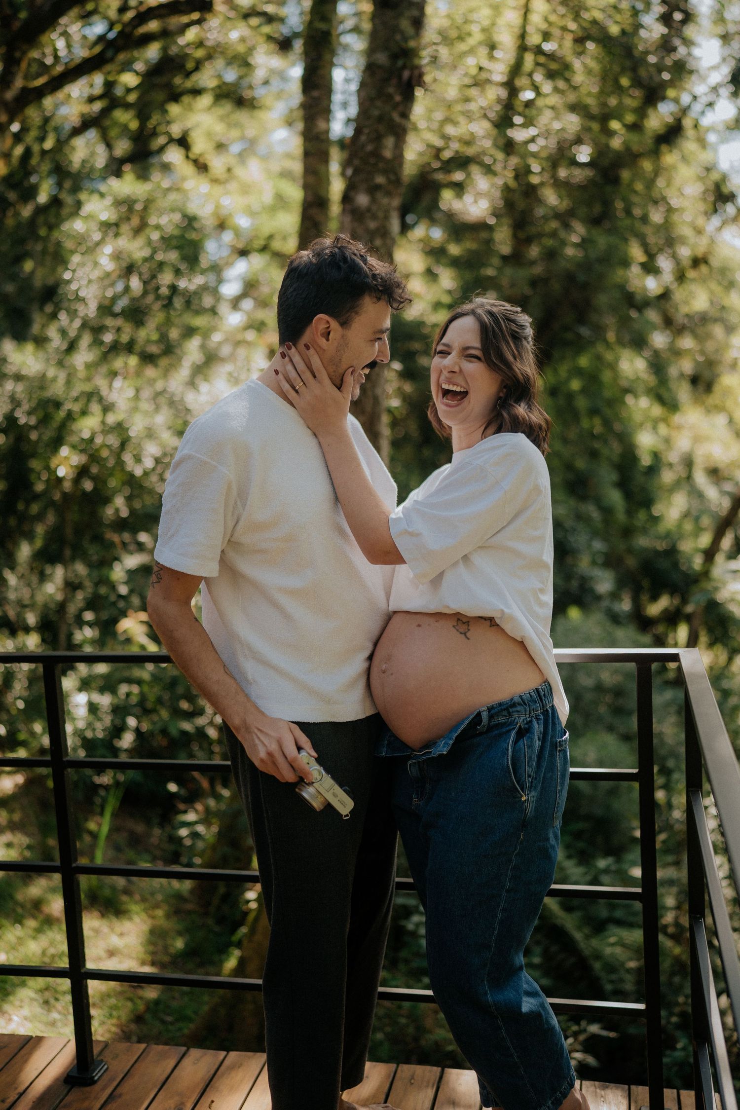 Joyful maternity moment captured on outdoor deck with forest backdrop.