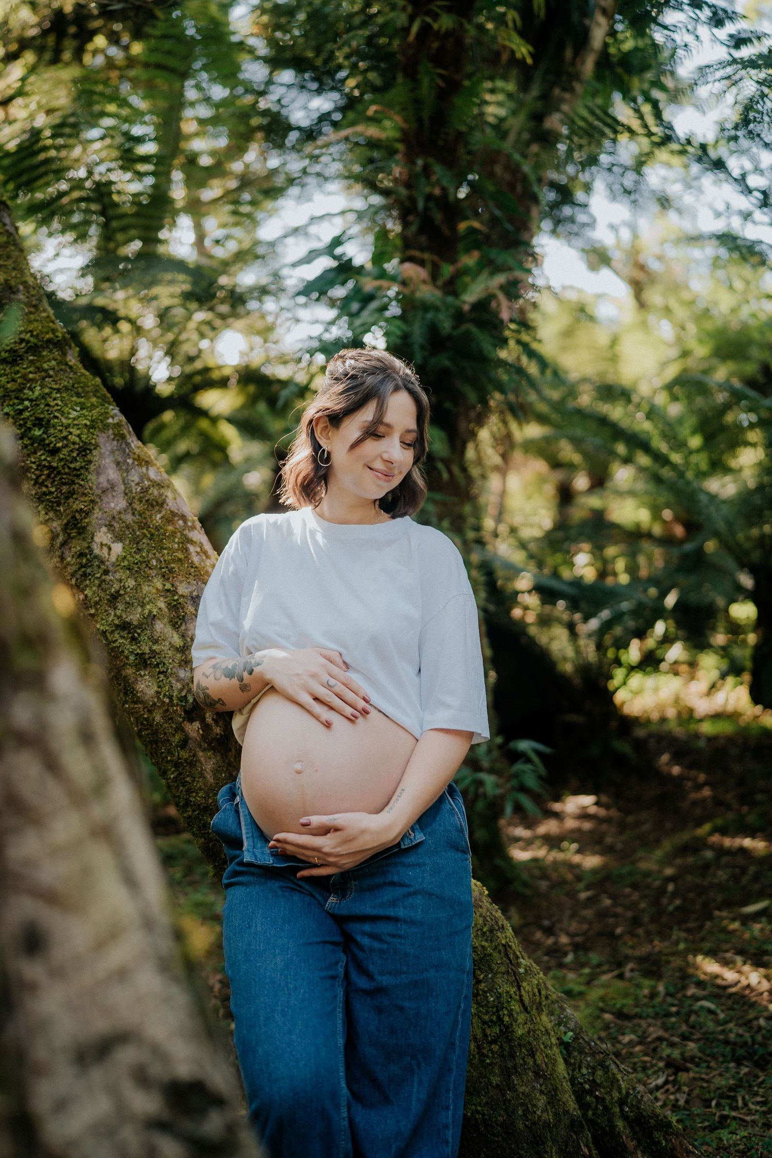 Peaceful maternity photo of expectant mother in natural forest setting with mossy trees.