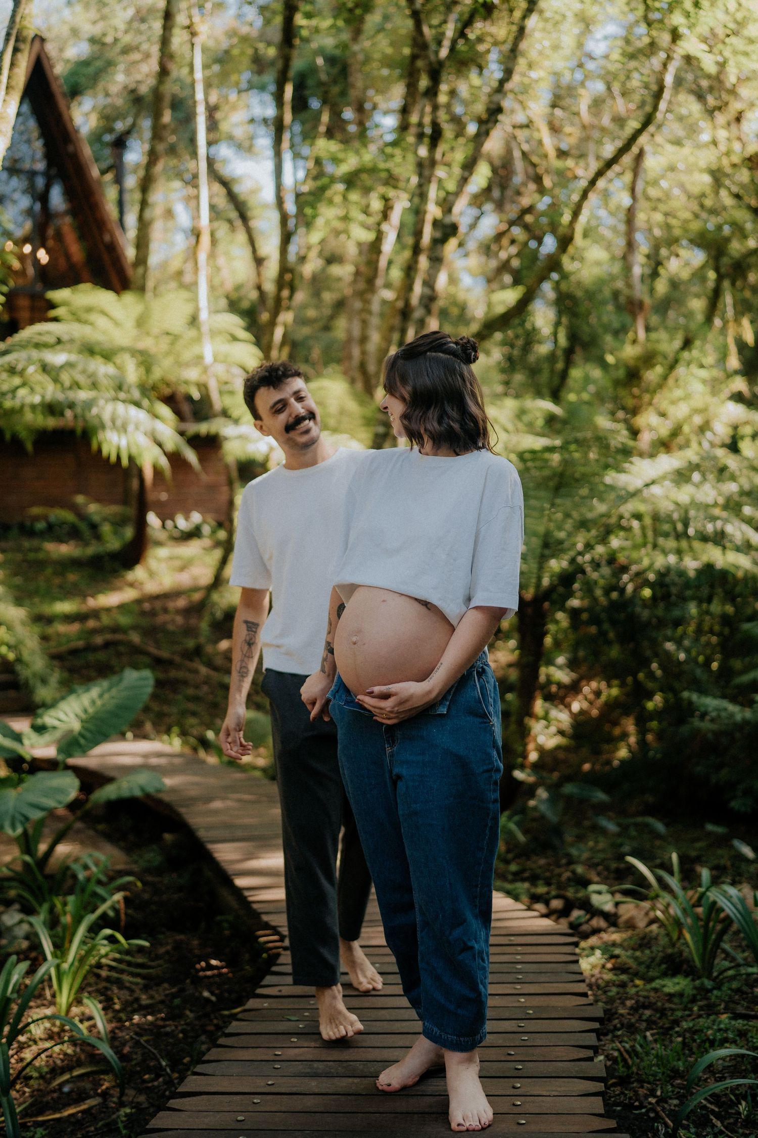Natural maternity photography on wooden boardwalk surrounded by lush forest greenery.