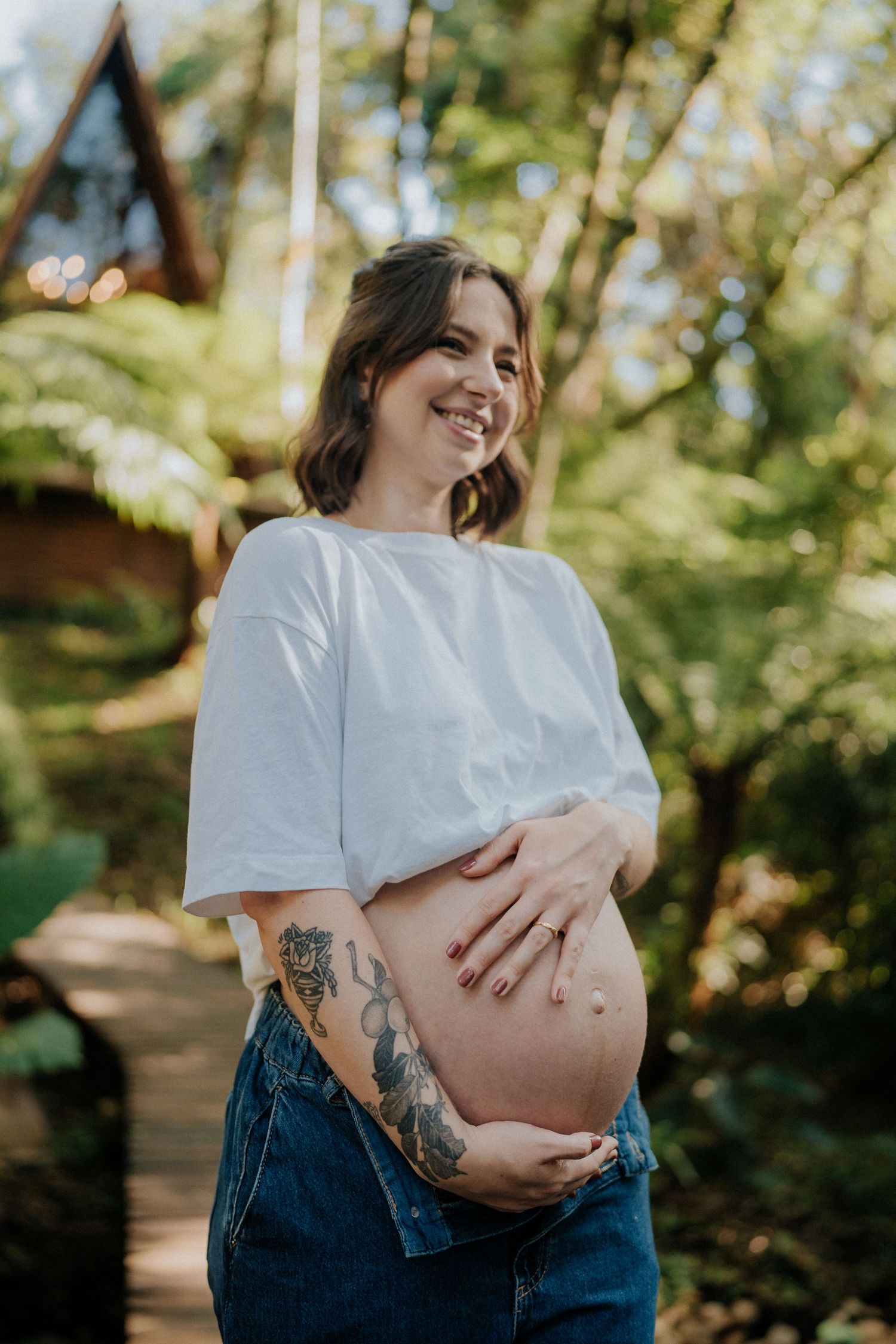 Outdoor maternity portrait showing expectant mother in white shirt with visible tattoo sleeve.
