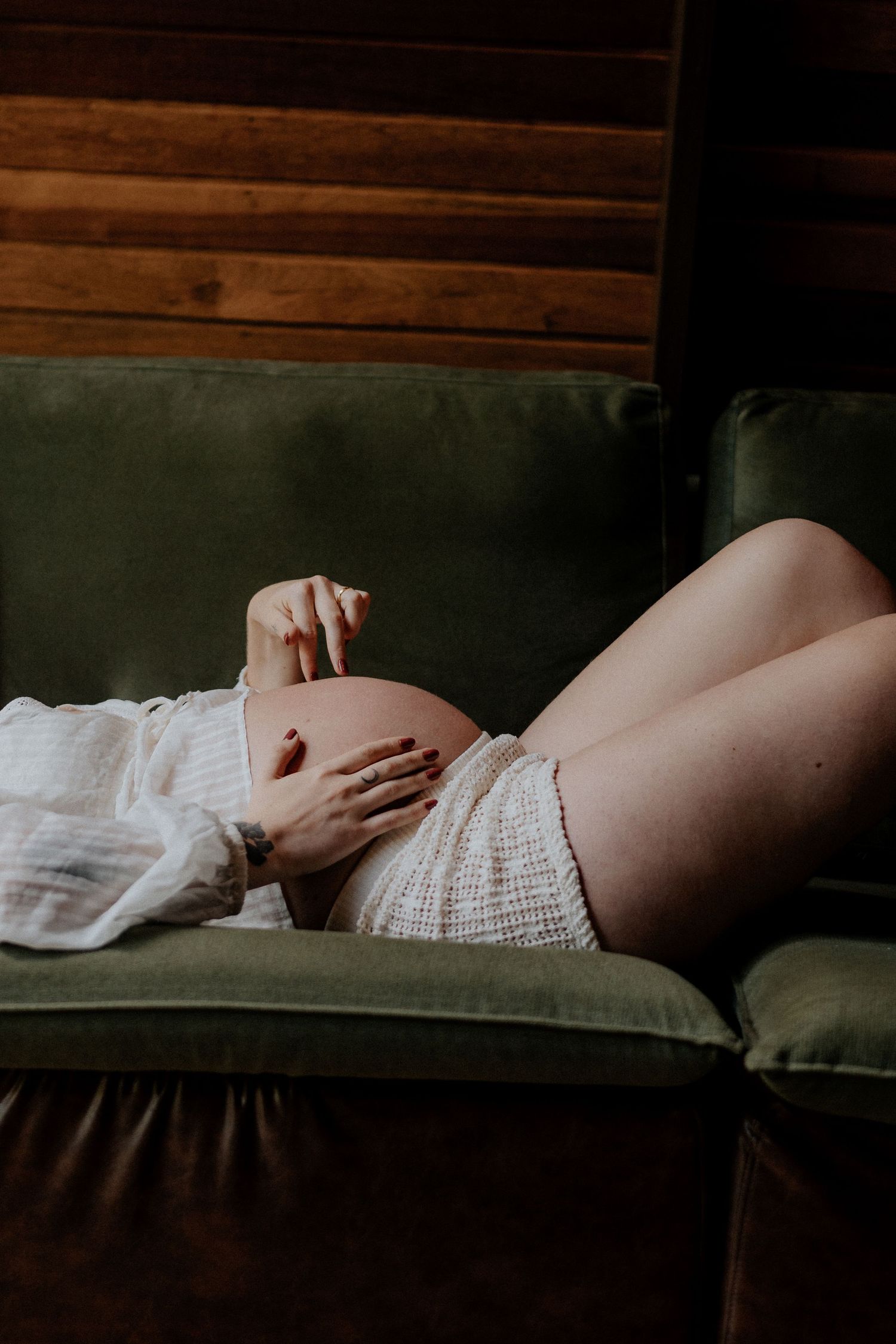 Artistic maternity photos with dramatic lighting on a dark green couch.