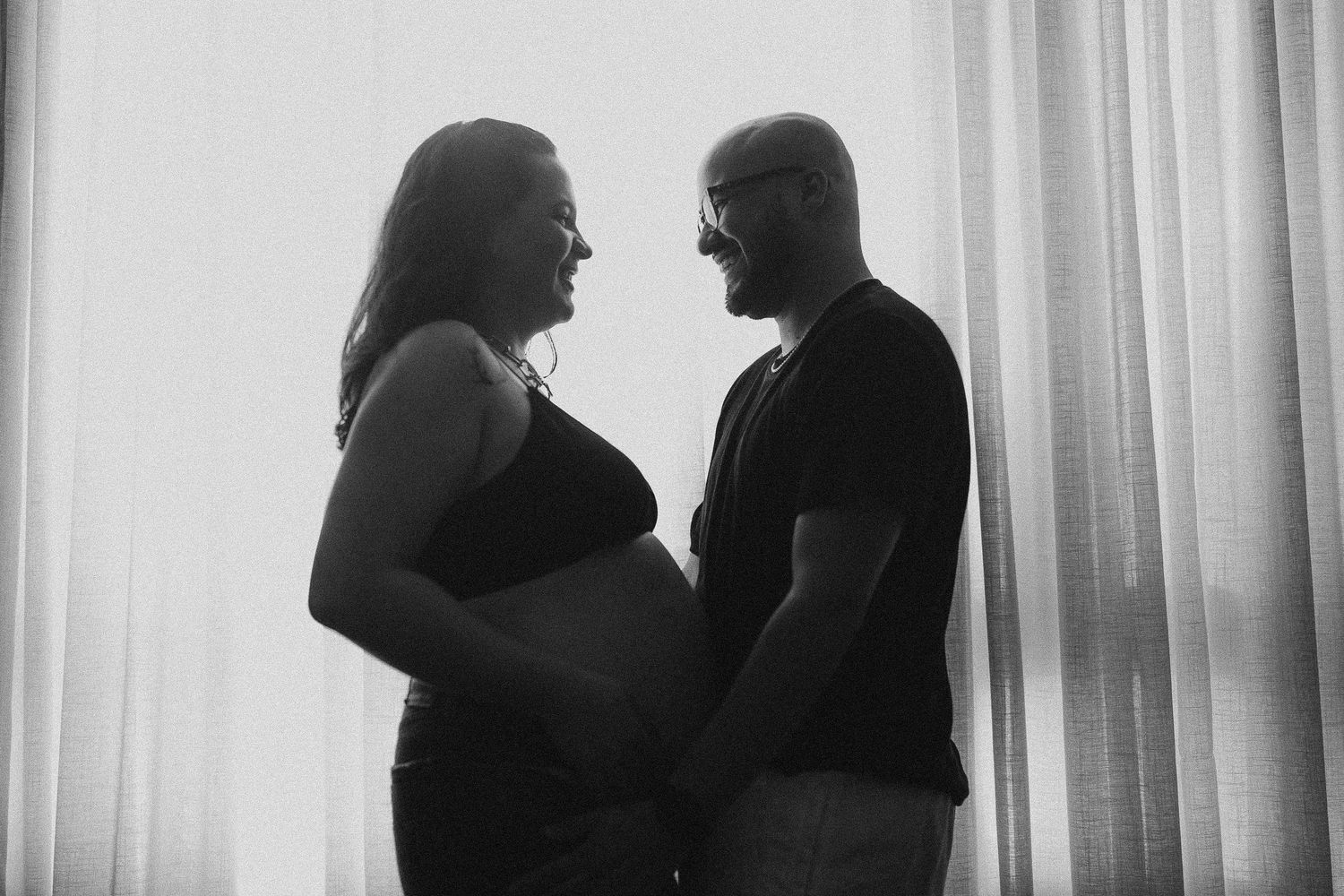 Silhouetted maternity portrait of couple by window in black and white.