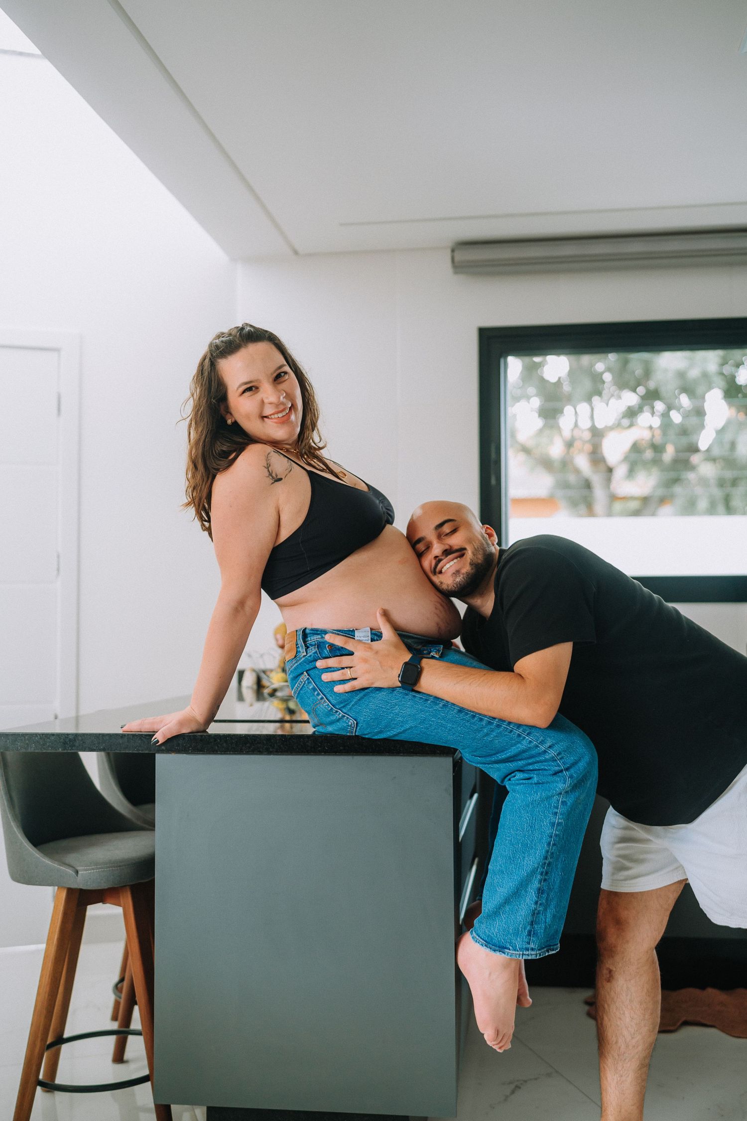 Playful maternity photo of couple by kitchen counter in bright modern space.