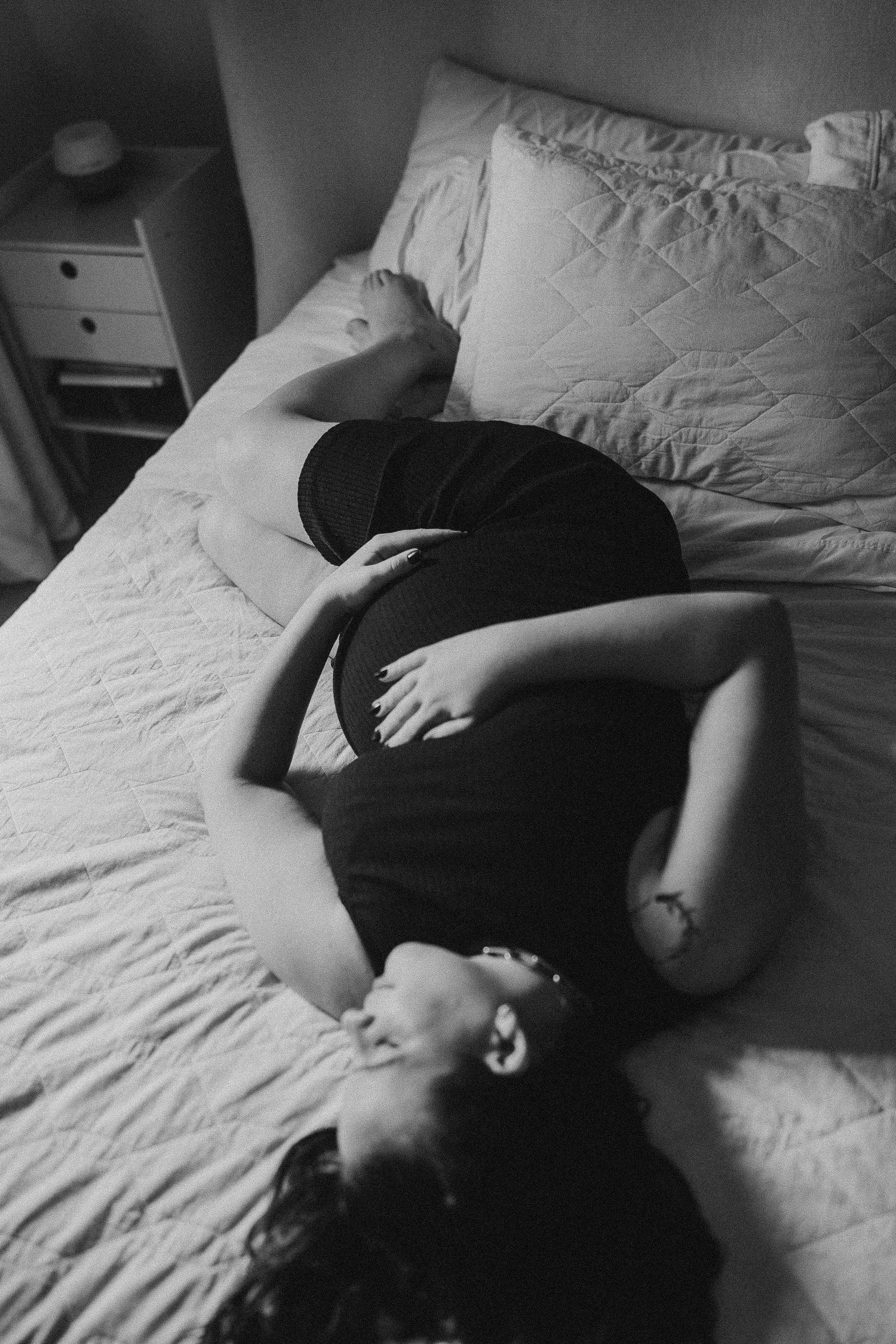 Black and white maternity photo of pregnant woman resting peacefully on bed.