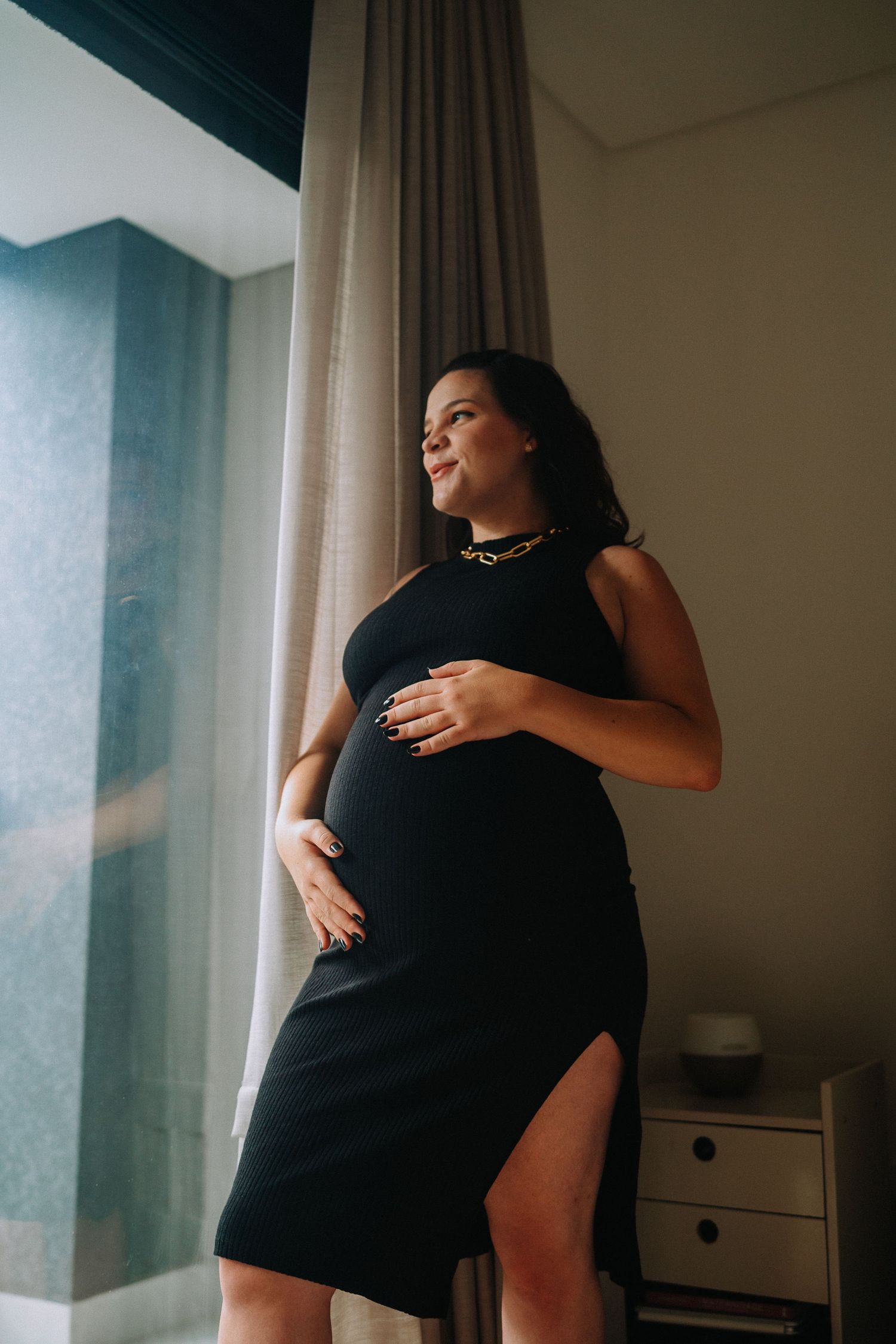 Elegant maternity photo featuring black dress with side slit in natural window light.