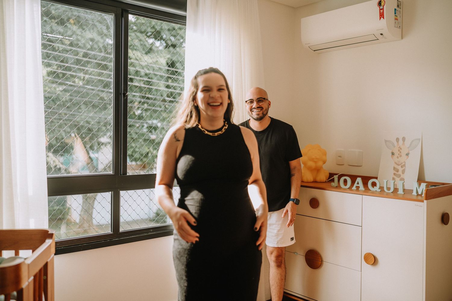 Maternity photo shoot in nursery room with couple standing by window.