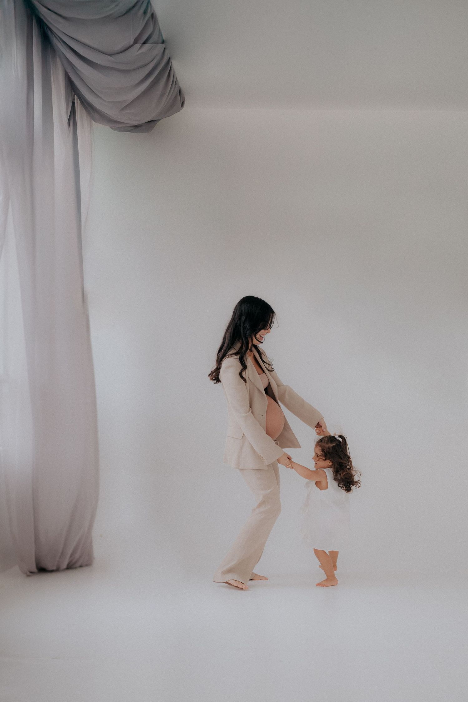 Parent and child dancing together in minimalist white studio setting.