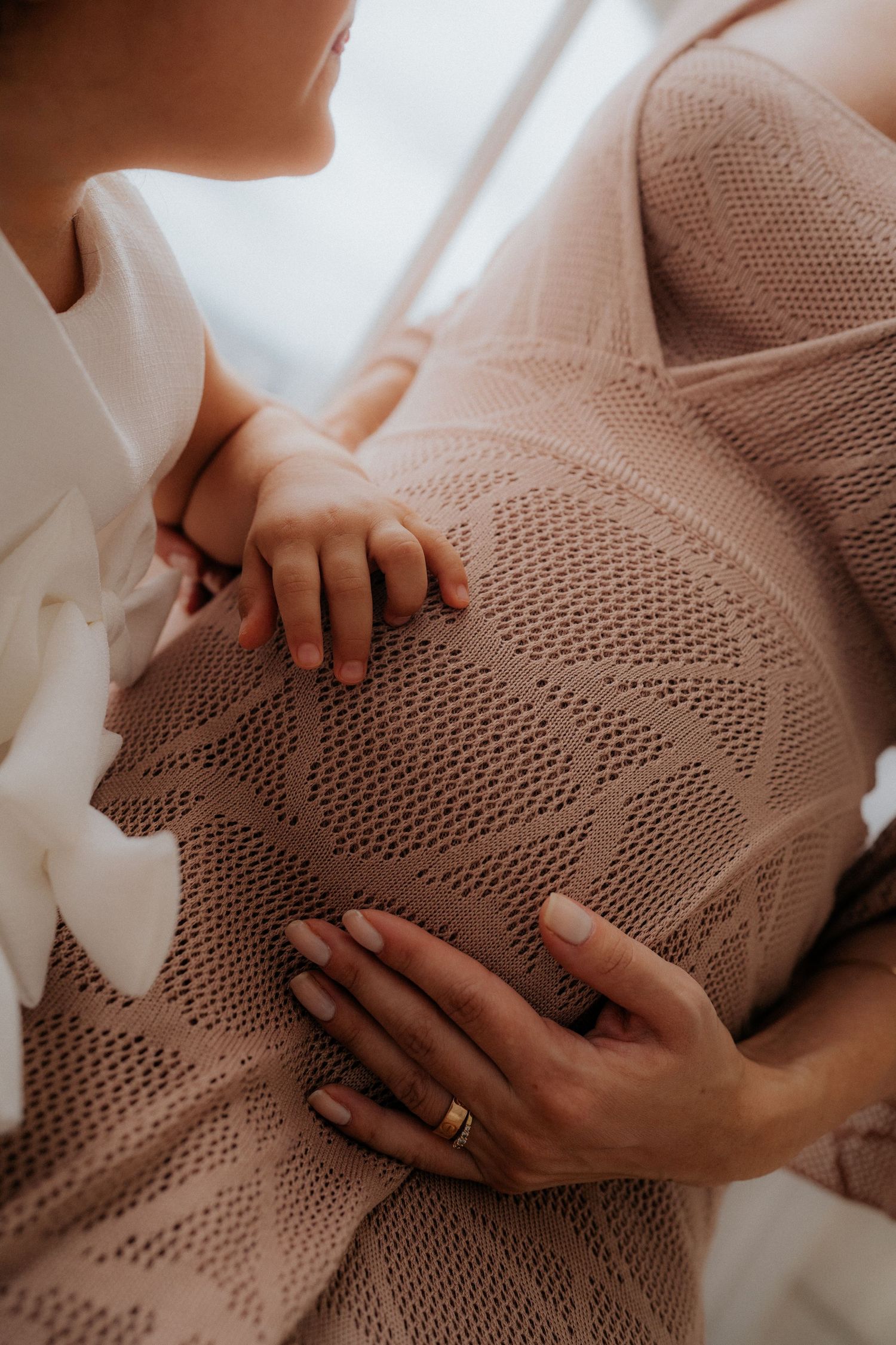Close-up maternity photo showing hands tenderly cradling a pregnant belly through knit fabric.