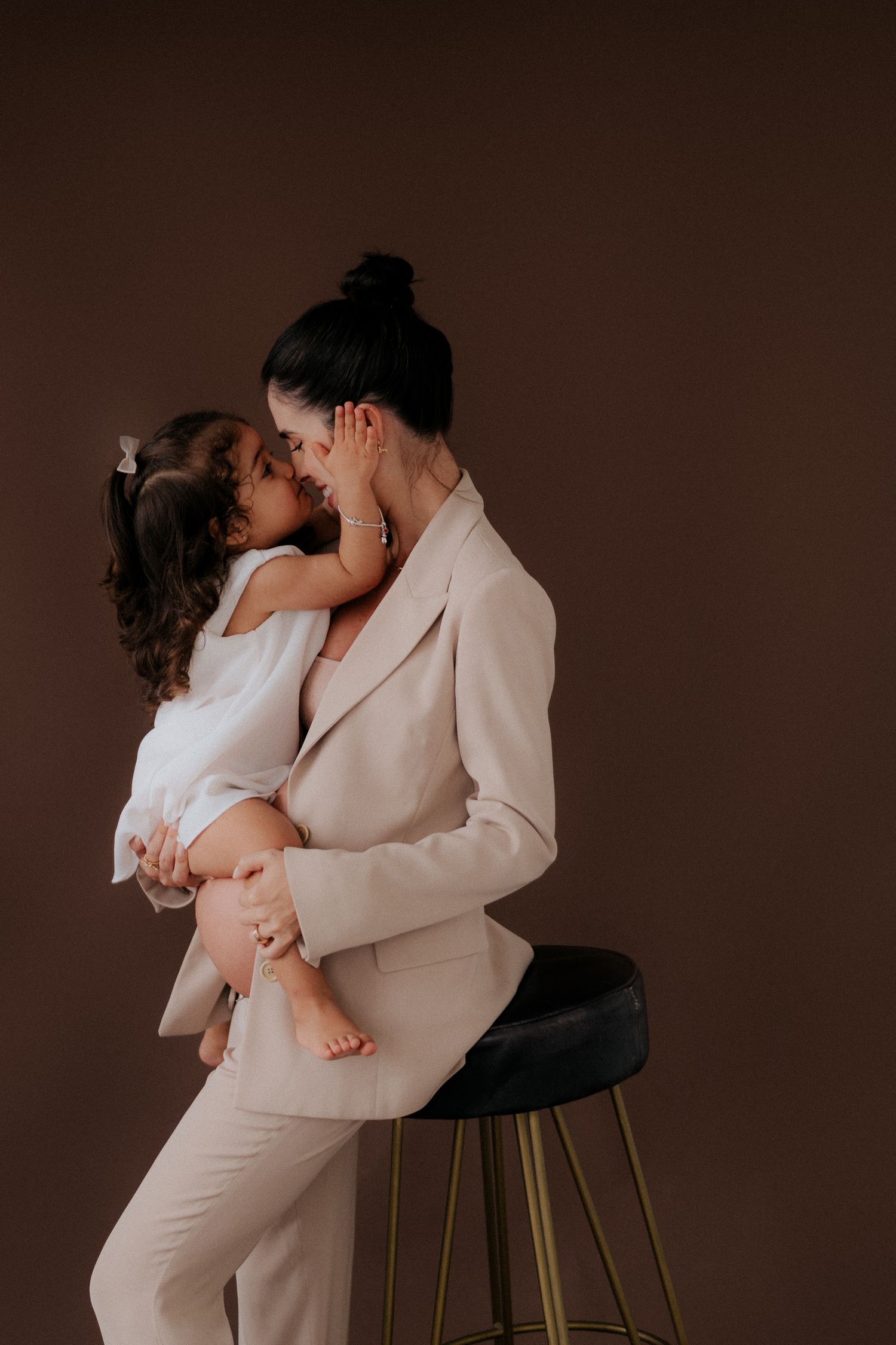 A tender moment captured between parent and child in a beige outfit against a brown backdrop.