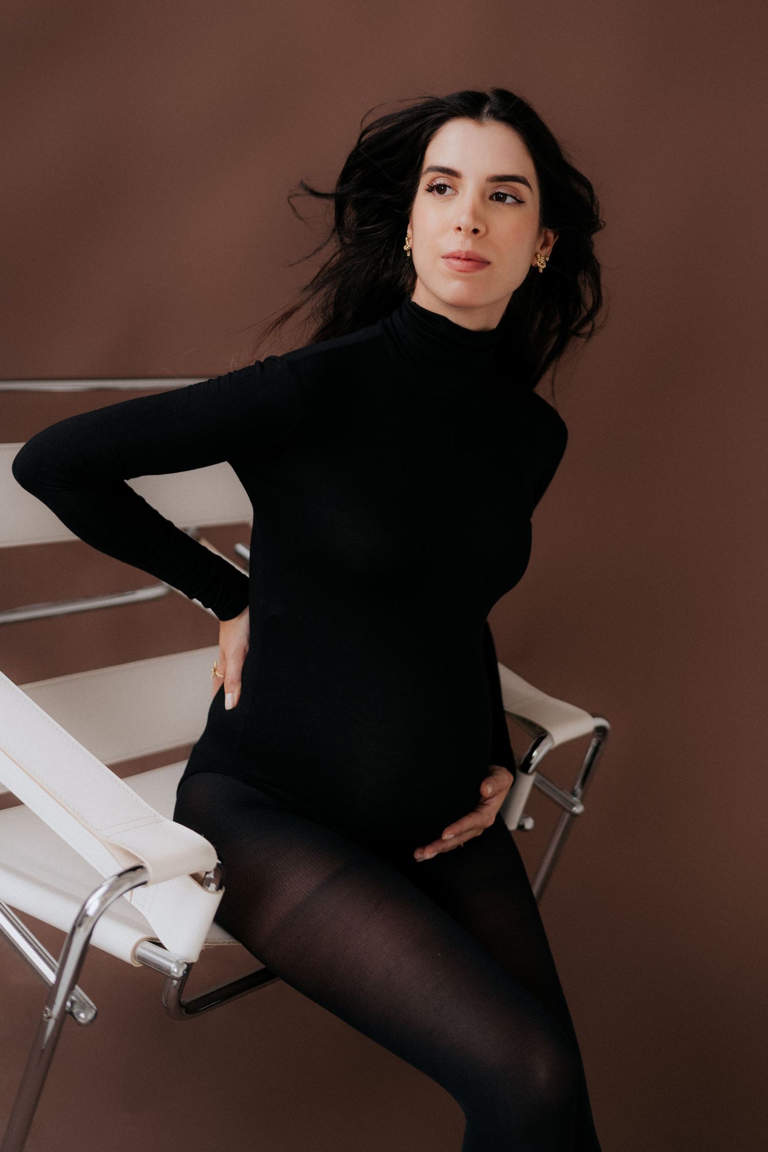 Maternity portrait featuring woman in black turtleneck against brown background.