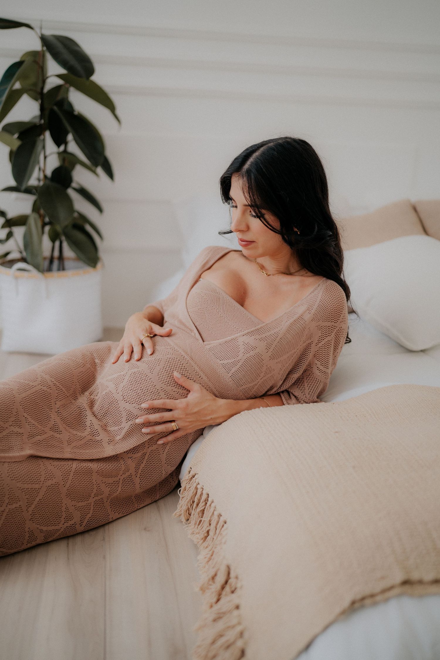 Expectant woman in blush dress rests peacefully on beige couch.
