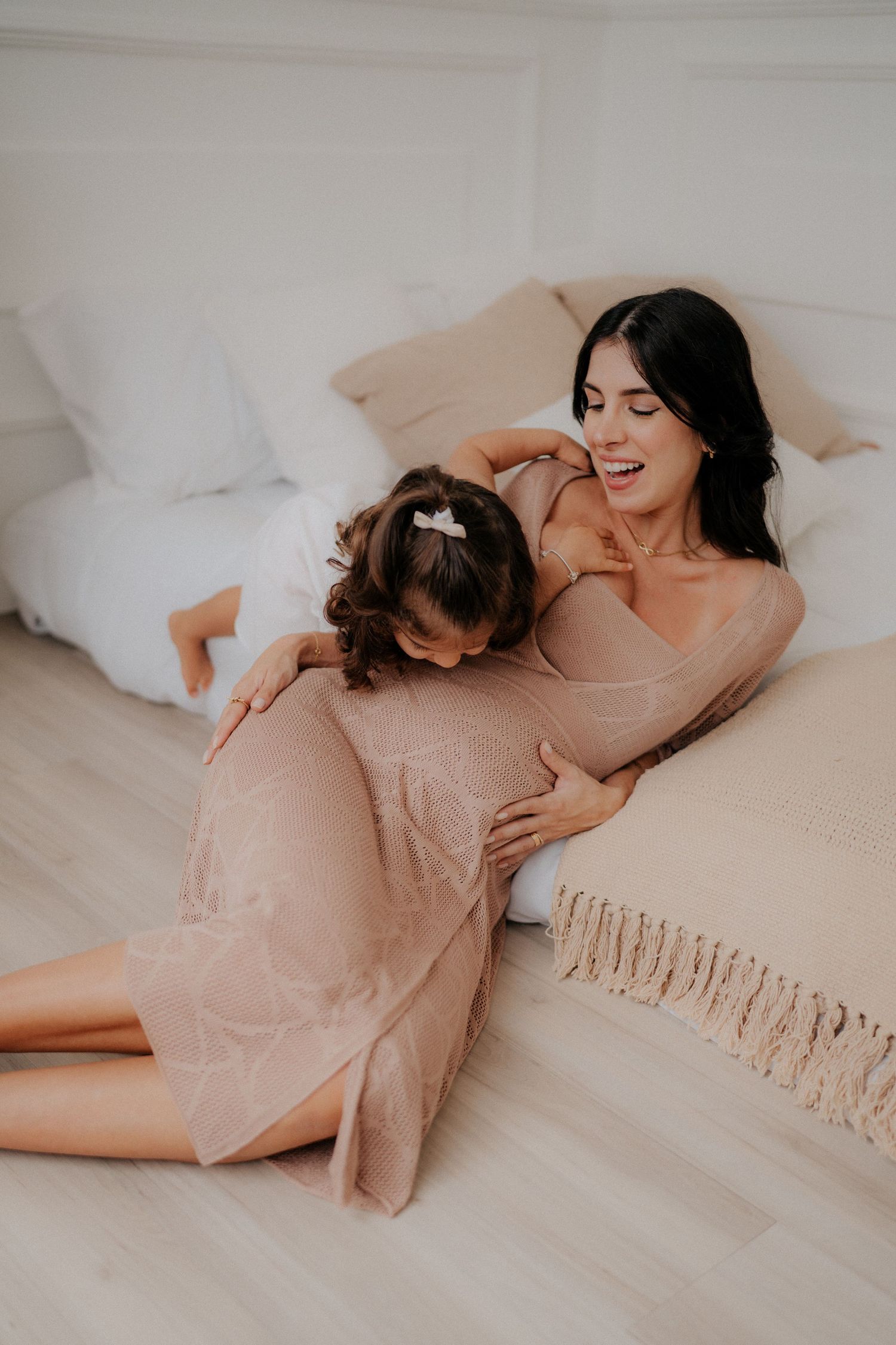 Mother and child share intimate moment on bed with soft lighting.